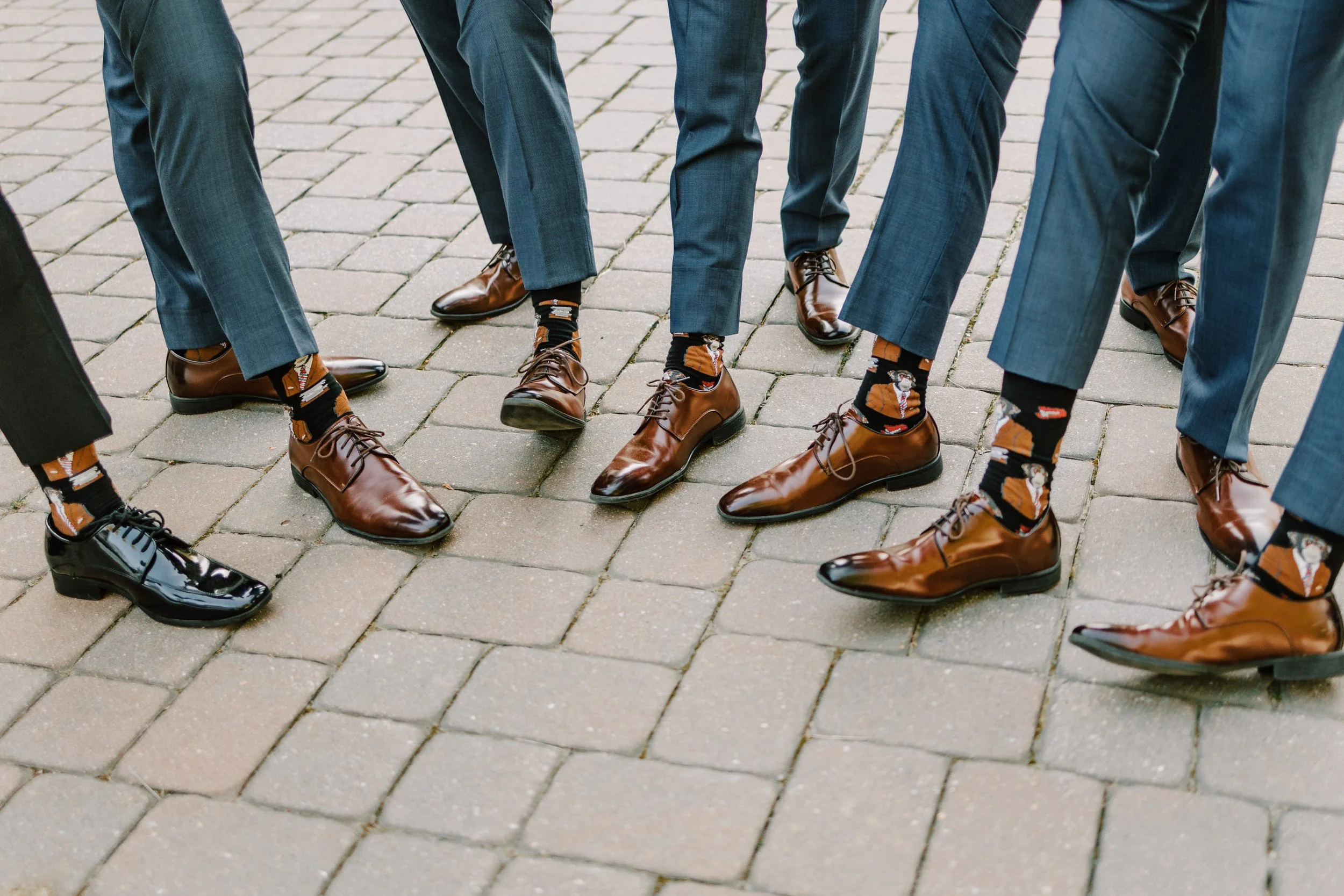 Men dressed in suits with colorful socks and polished leather shoes standing on a brick sidewalk.