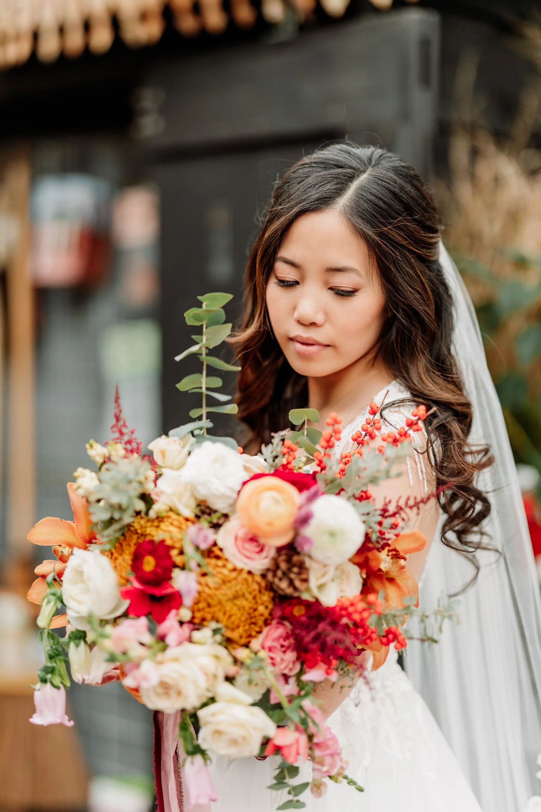 A bride holding a colorful bouquet of flowers with greenery, in an outdoor setting.