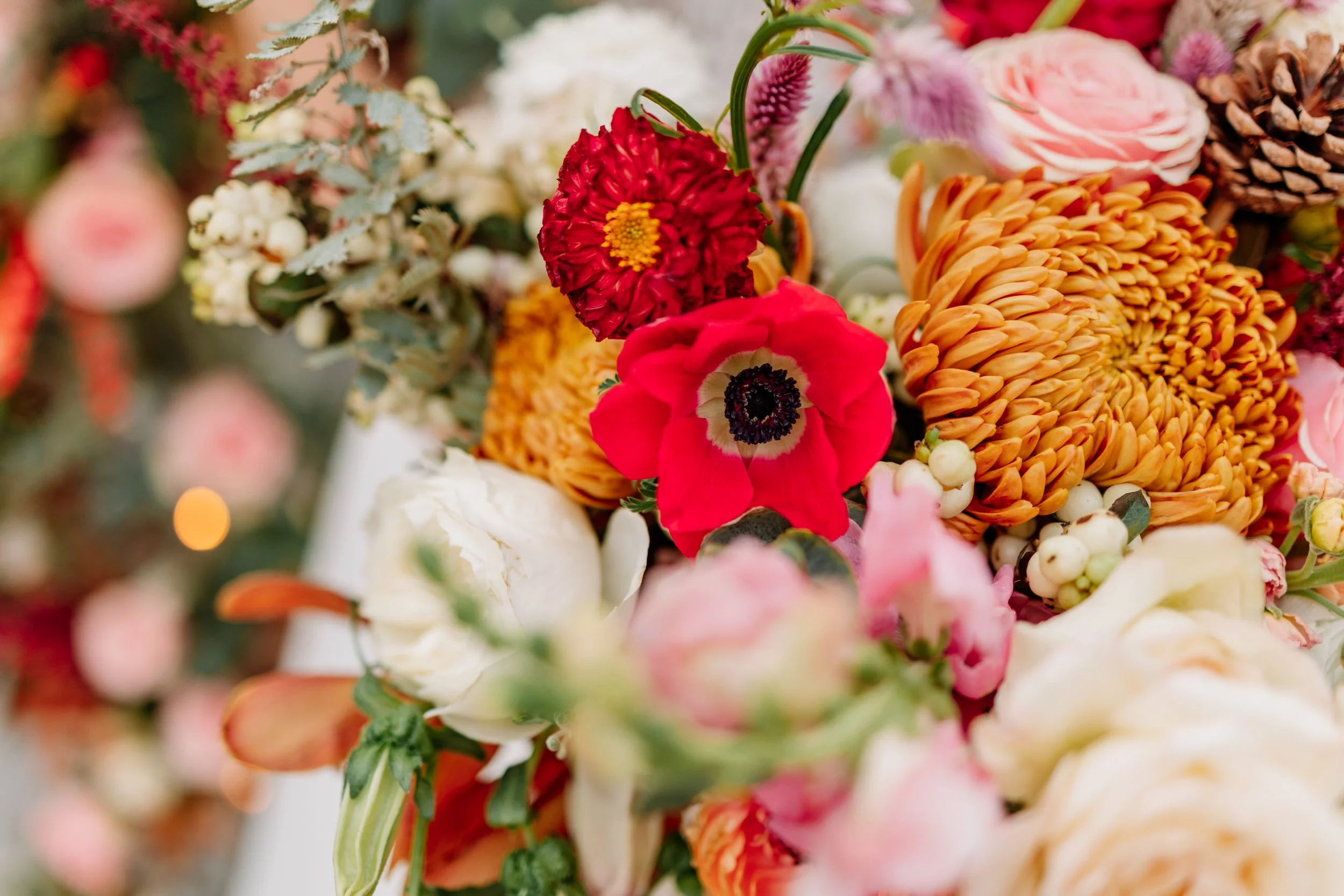 Close-up of a colorful bouquet featuring red anemone, orange chrysanthemum, pink ranunculus, and various white and pink flowers.