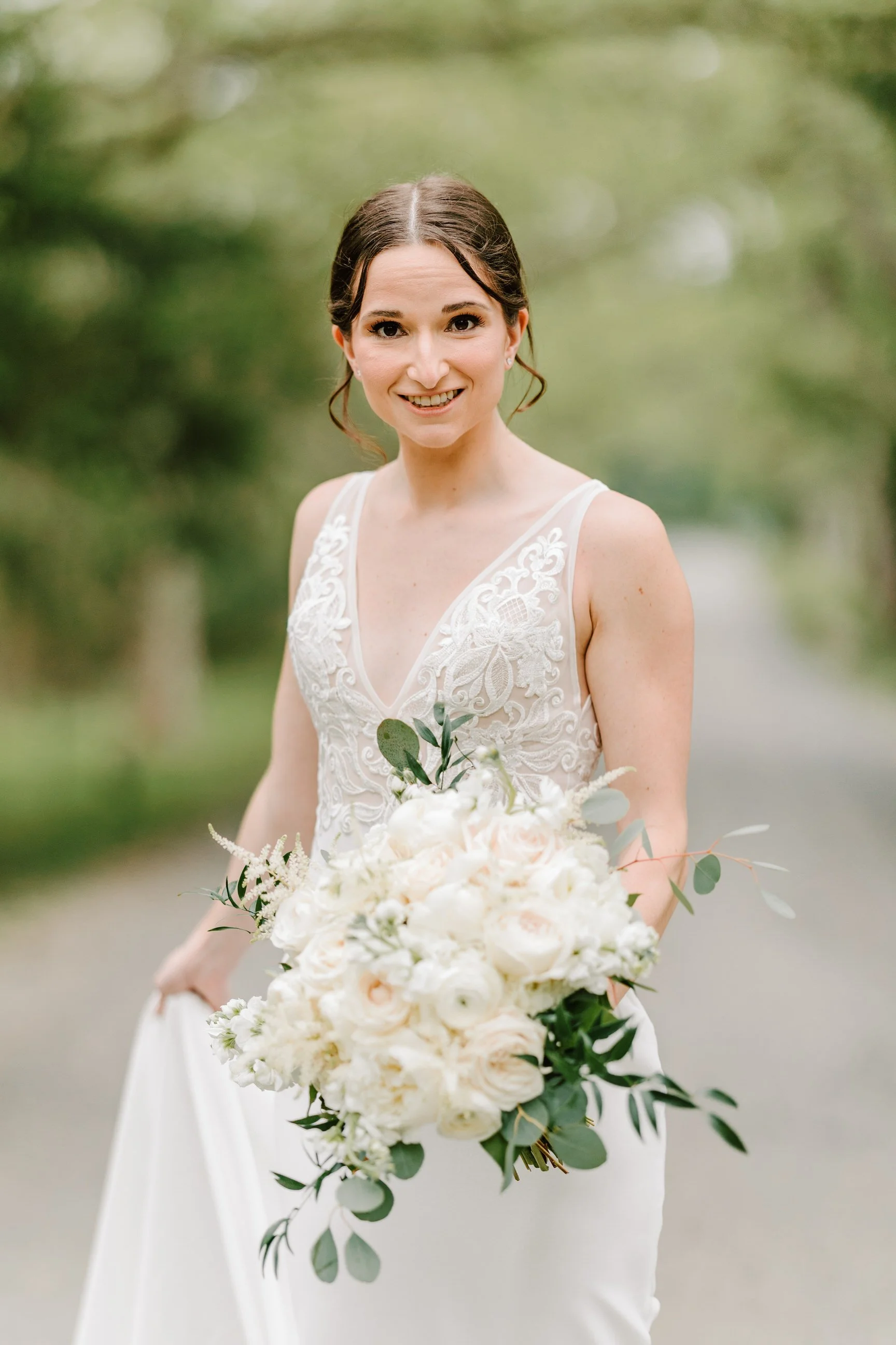 A bride in a white dress holding a bouquet of white and blush pink flowers outdoors.