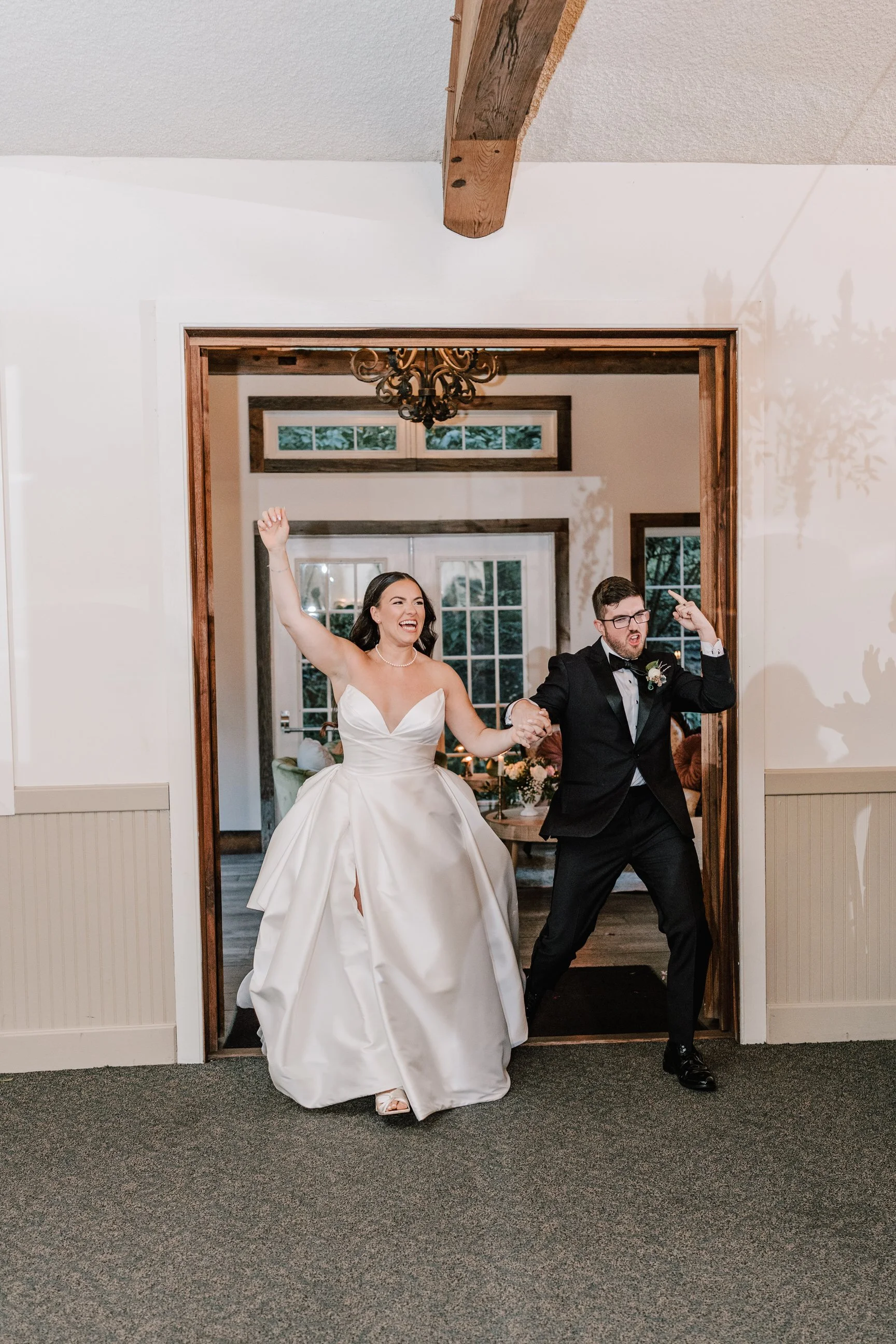 Bride in a white wedding gown and groom in a black tuxedo celebrating as they walk through a doorway.