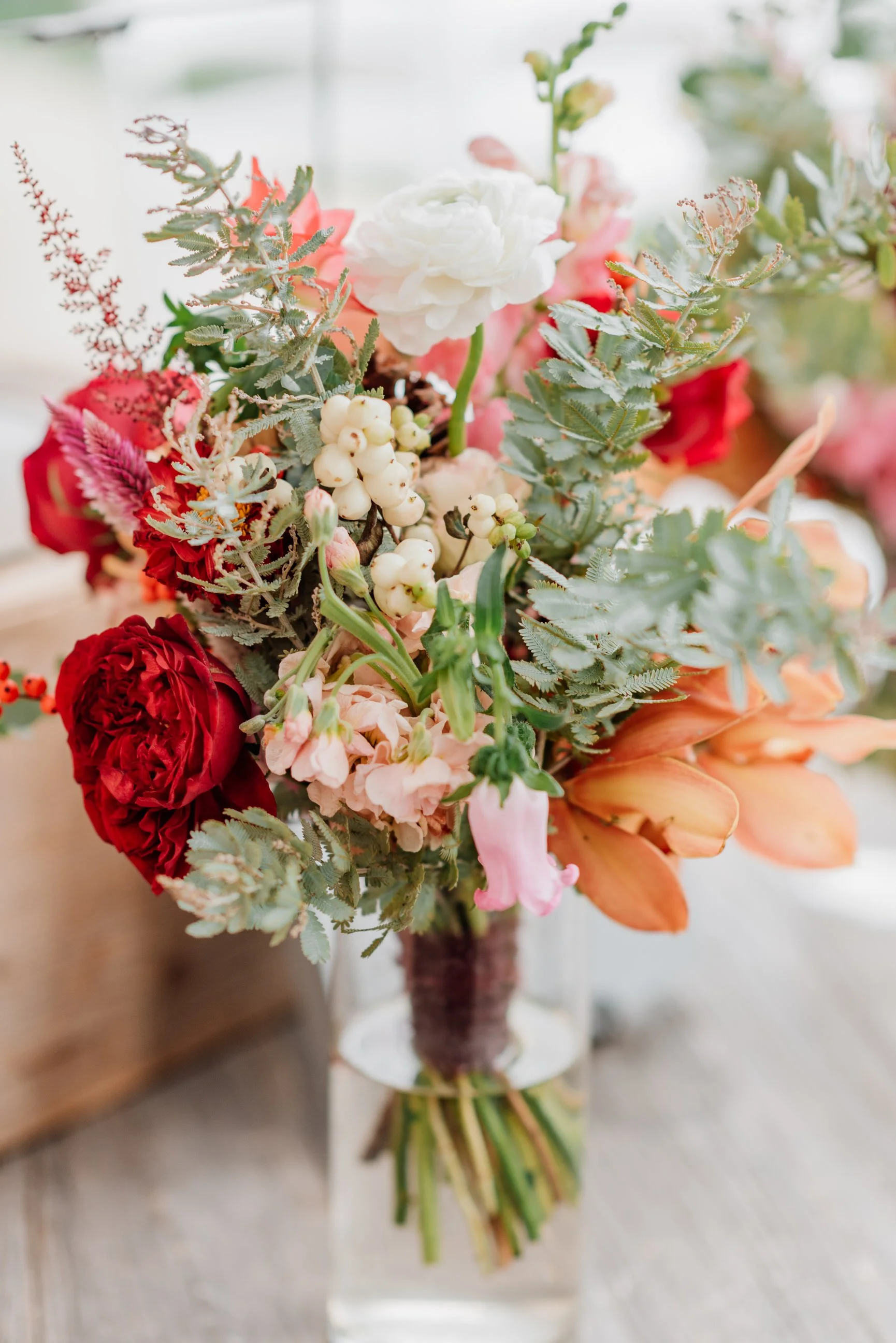 A colorful bouquet of assorted flowers and greenery in a clear glass vase on a wooden surface.