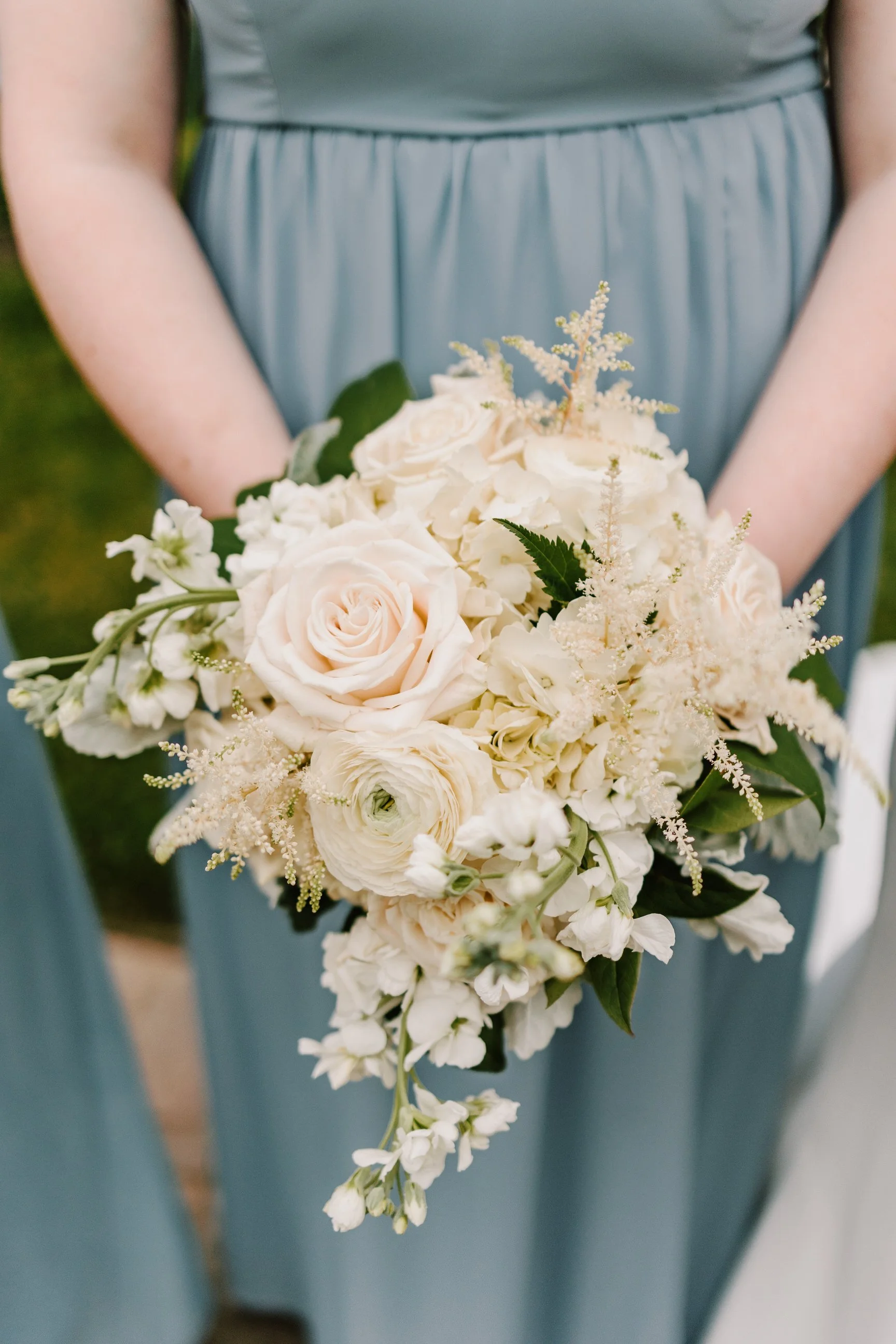 Person holding a bouquet of white and cream flowers, including roses, in formal attire at a wedding or special event.