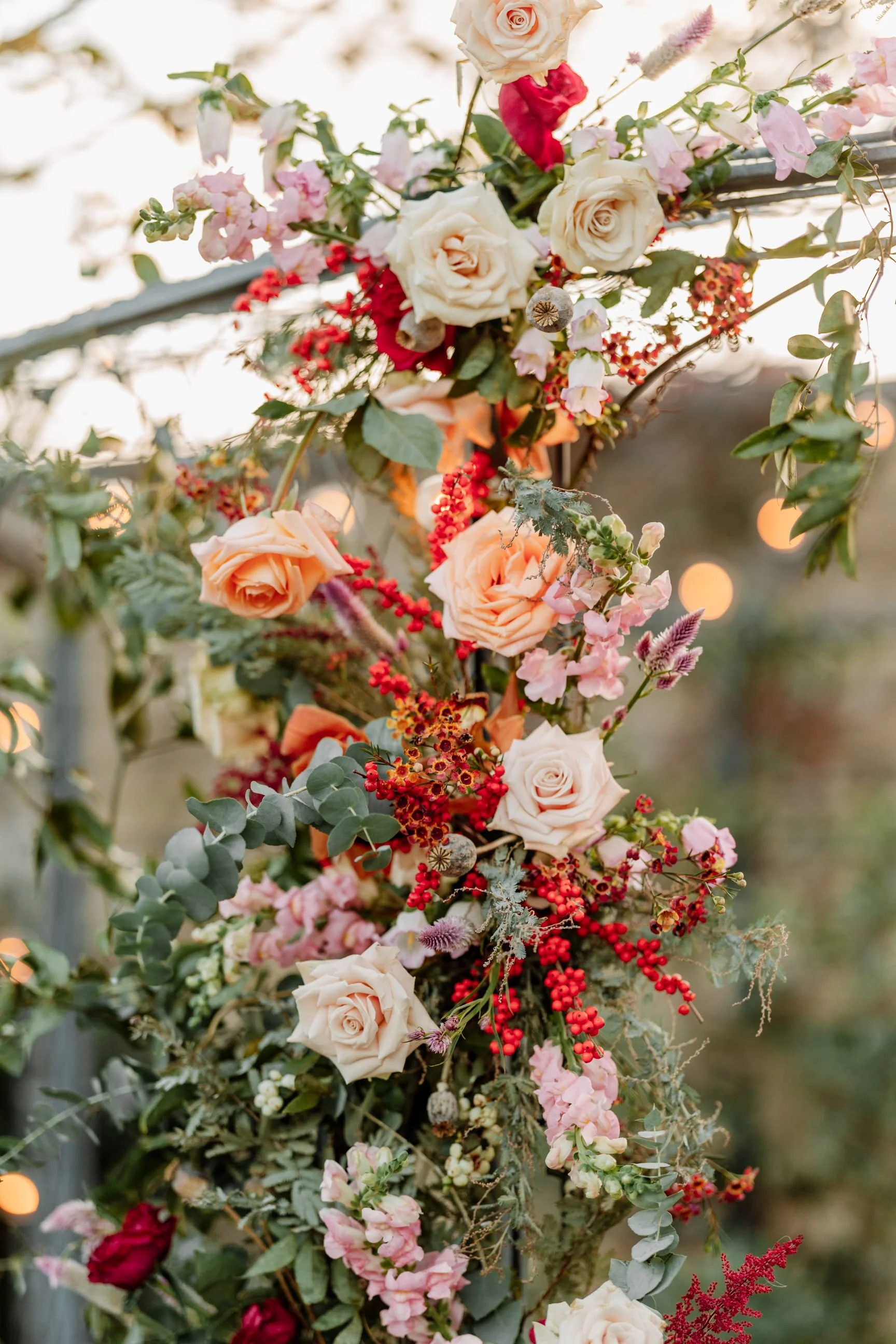 Close-up of an arrangement of roses, berries, and various flowers on a garden arch during sunset.