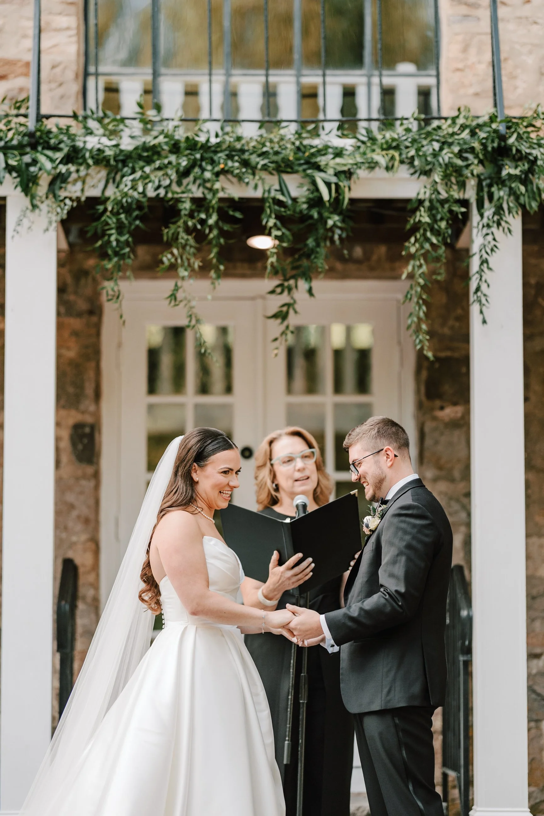 Bride and groom holding hands during wedding ceremony with officiant reading from a book