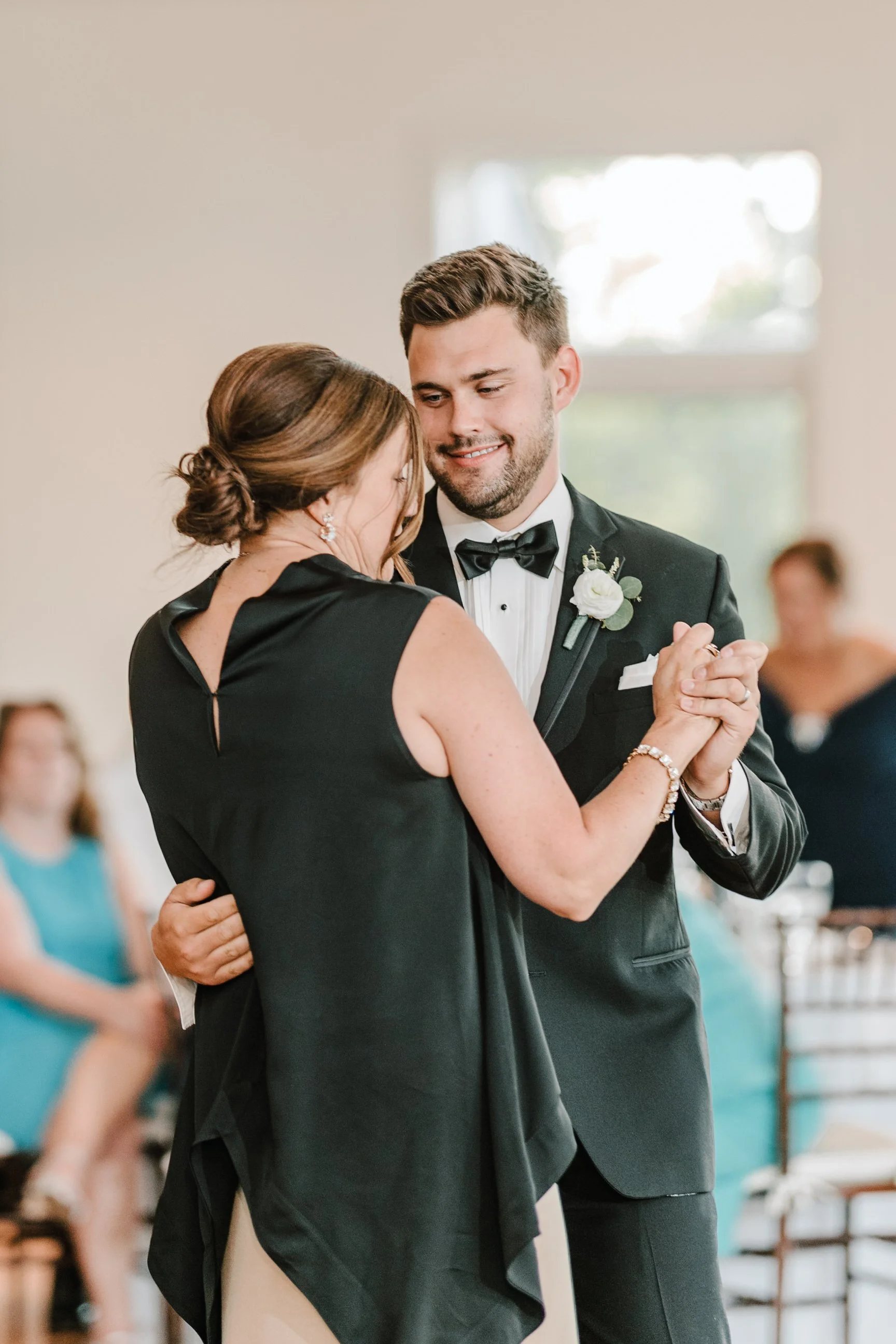 A man and woman dancing at a wedding, with the man in a tuxedo and the woman in a black dress.