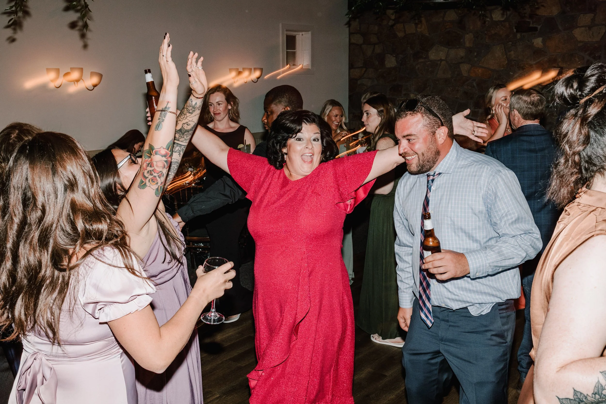 Happy woman in a red dress dancing with arms raised, surrounded by people at a celebration or party.