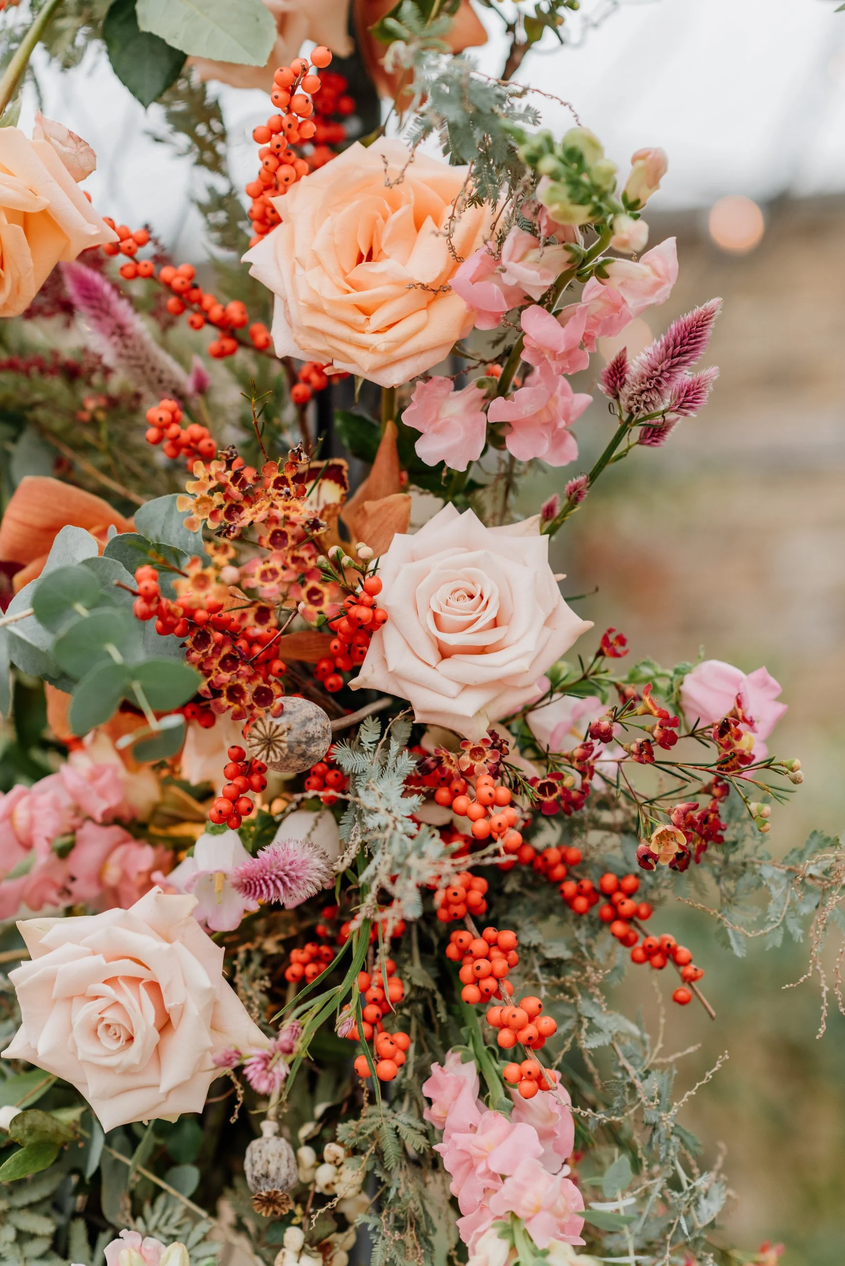 Close-up of a colorful floral arrangement with peach roses, pink snapdragons, orange berries, and various greenery.