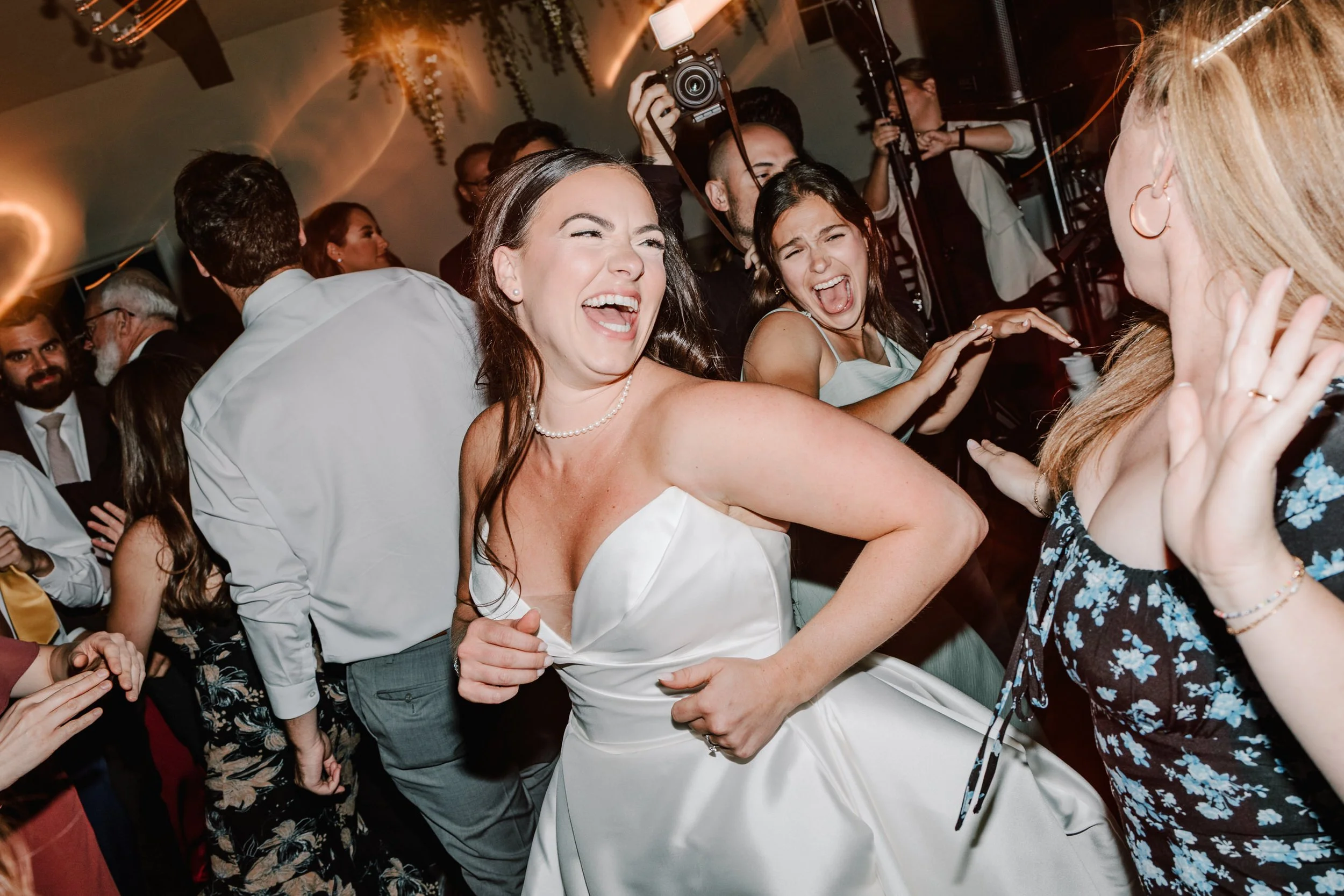 People dancing and celebrating at a wedding reception, with a woman in a white dress at the center.