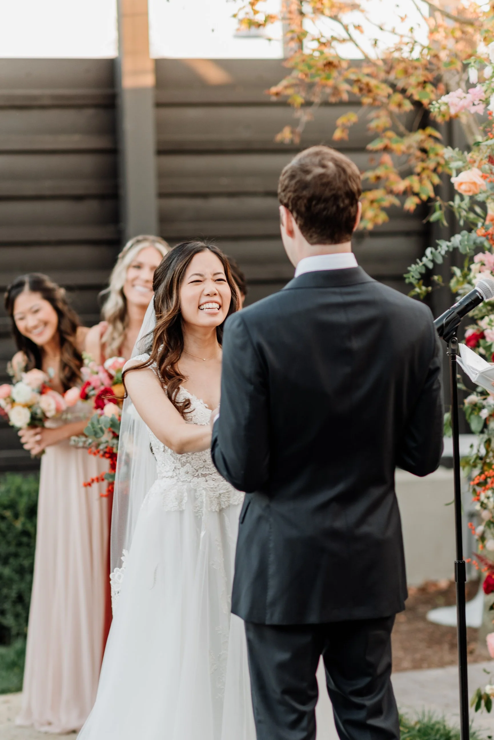 A bride and groom exchange vows during an outdoor wedding ceremony, with bridesmaids holding bouquets in the background.