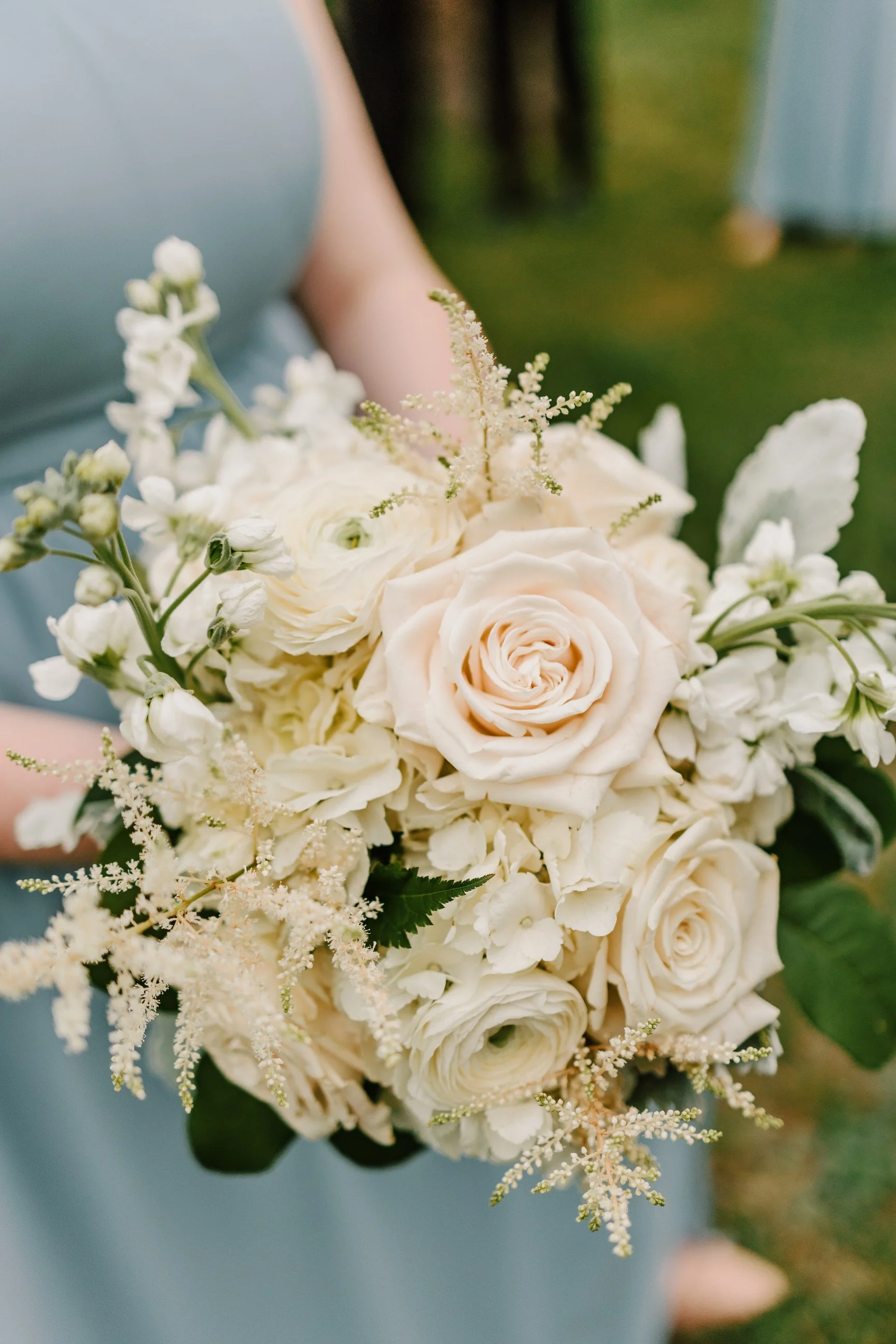 A person holding a bouquet of white and cream-colored roses and other white flowers.