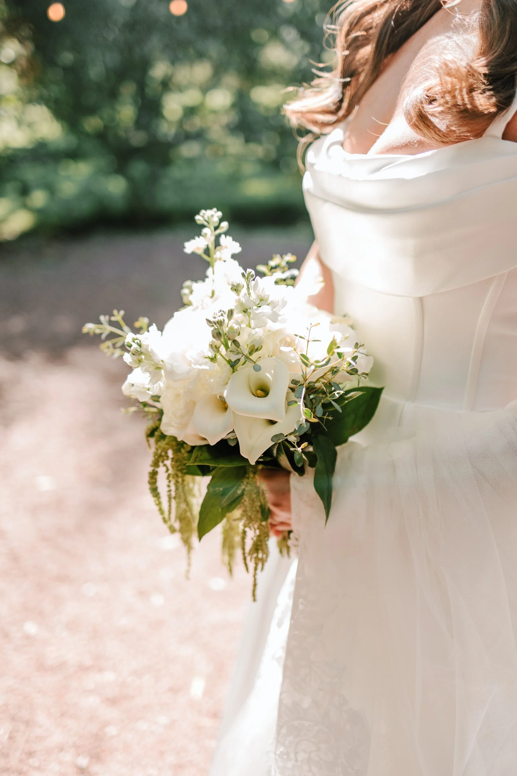A bride holding a bouquet of white flowers and greenery outdoors on a sunny day.