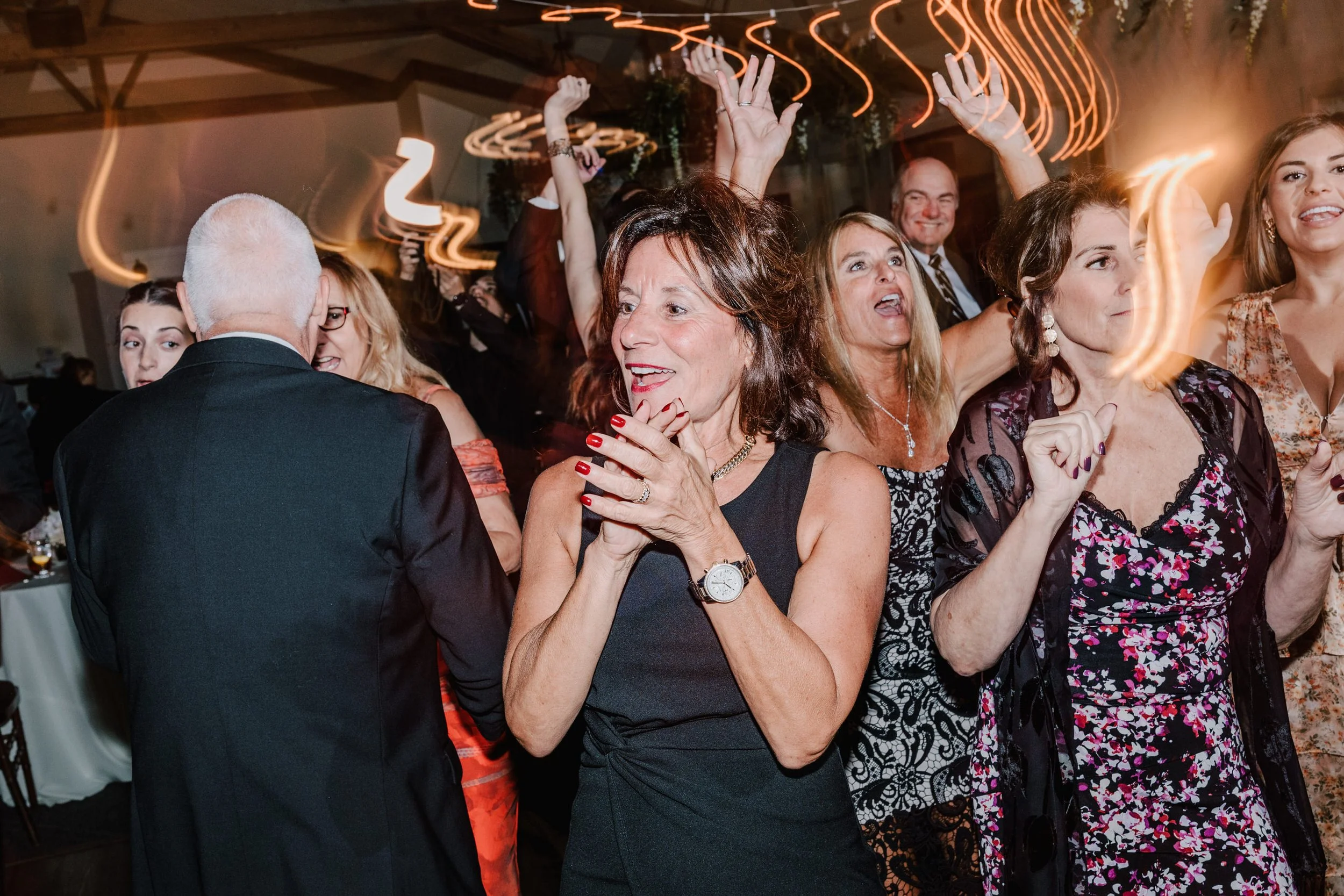 A group of people dancing and celebrating at a party or wedding reception, with light trails from the camera capturing their movements.