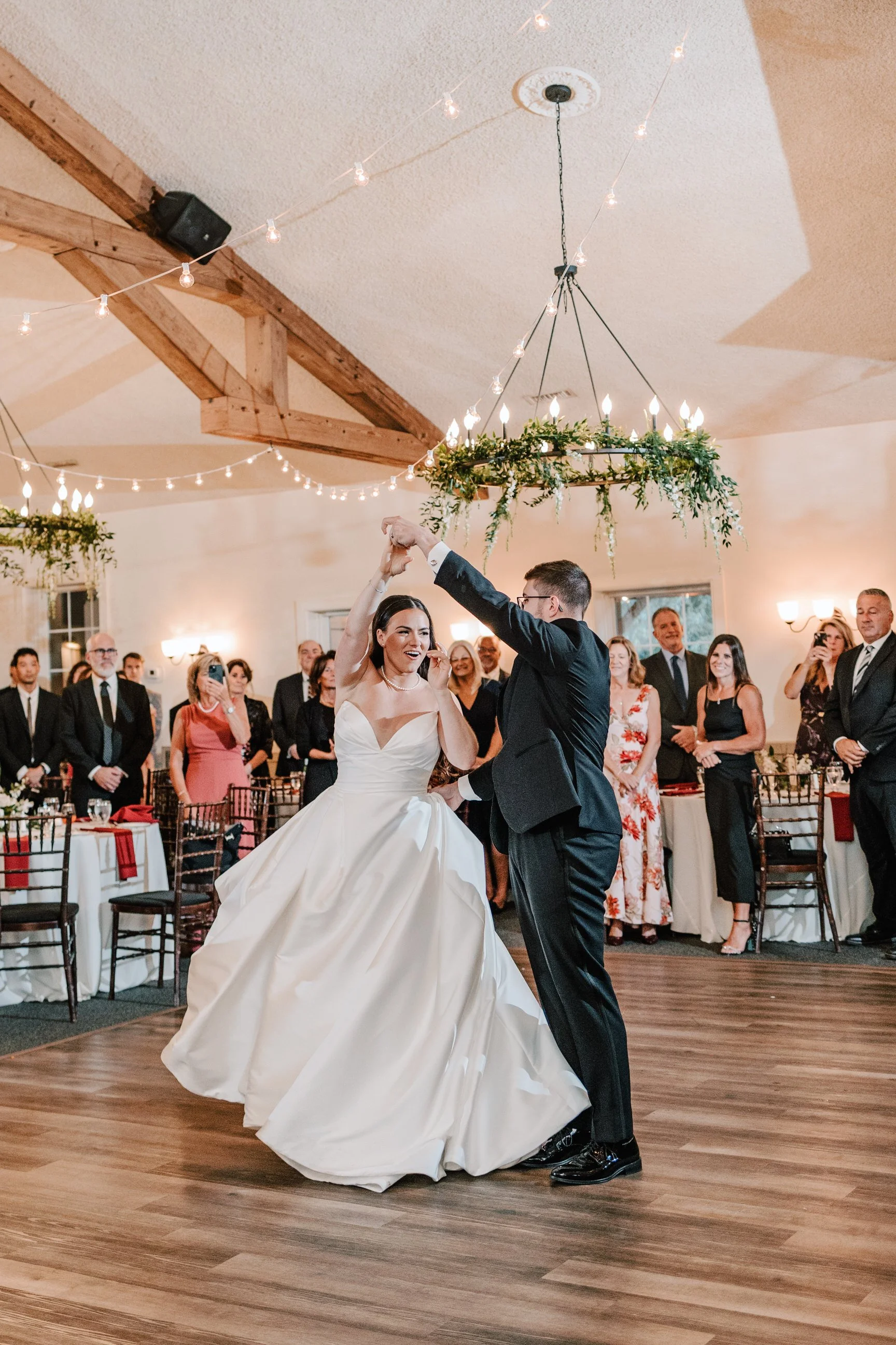 A bride and groom dancing at their wedding reception, surrounded by guests who are watching and smiling.