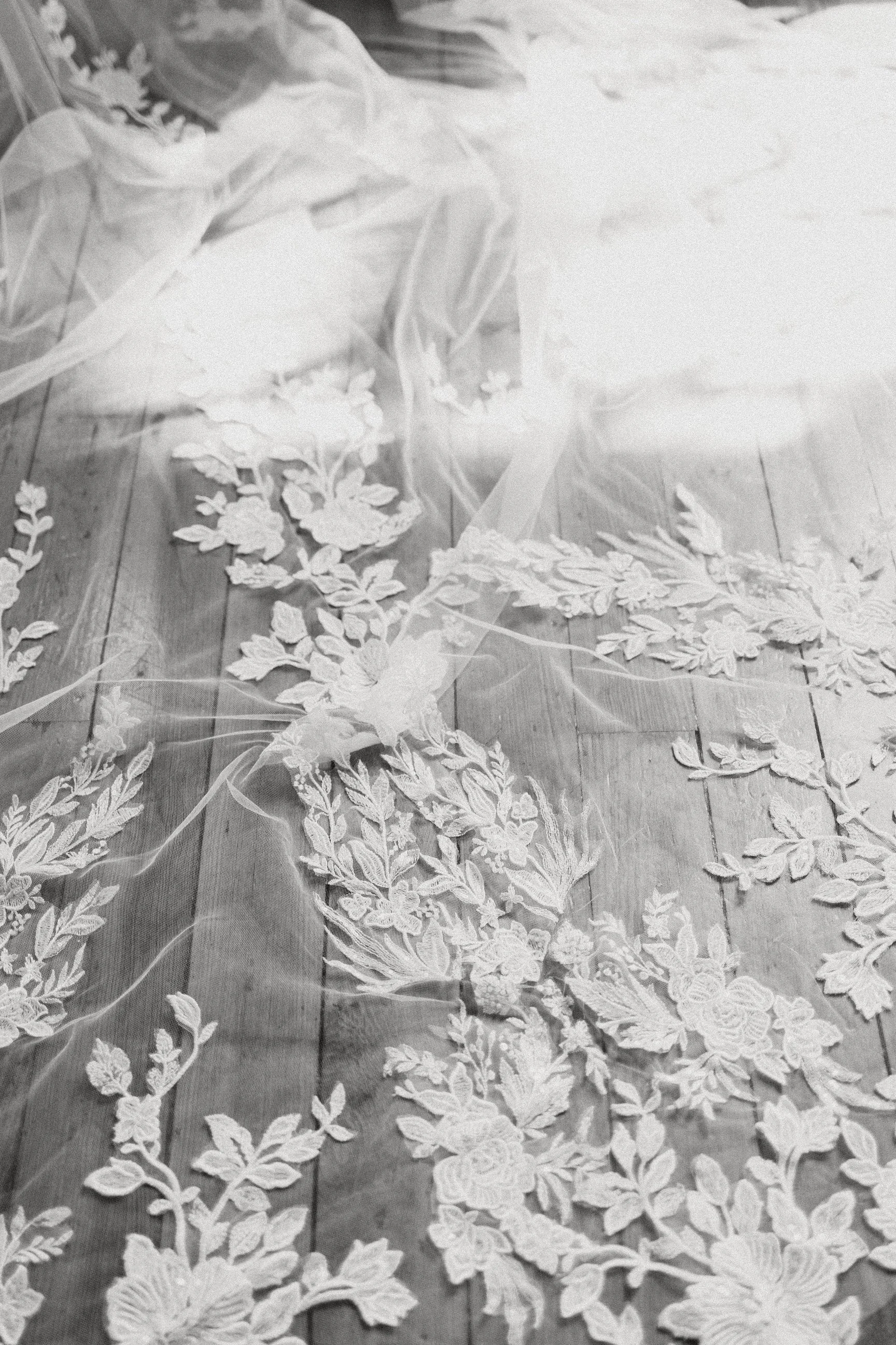 A delicate lace veil with intricate floral embroidery laid out on a wooden surface.