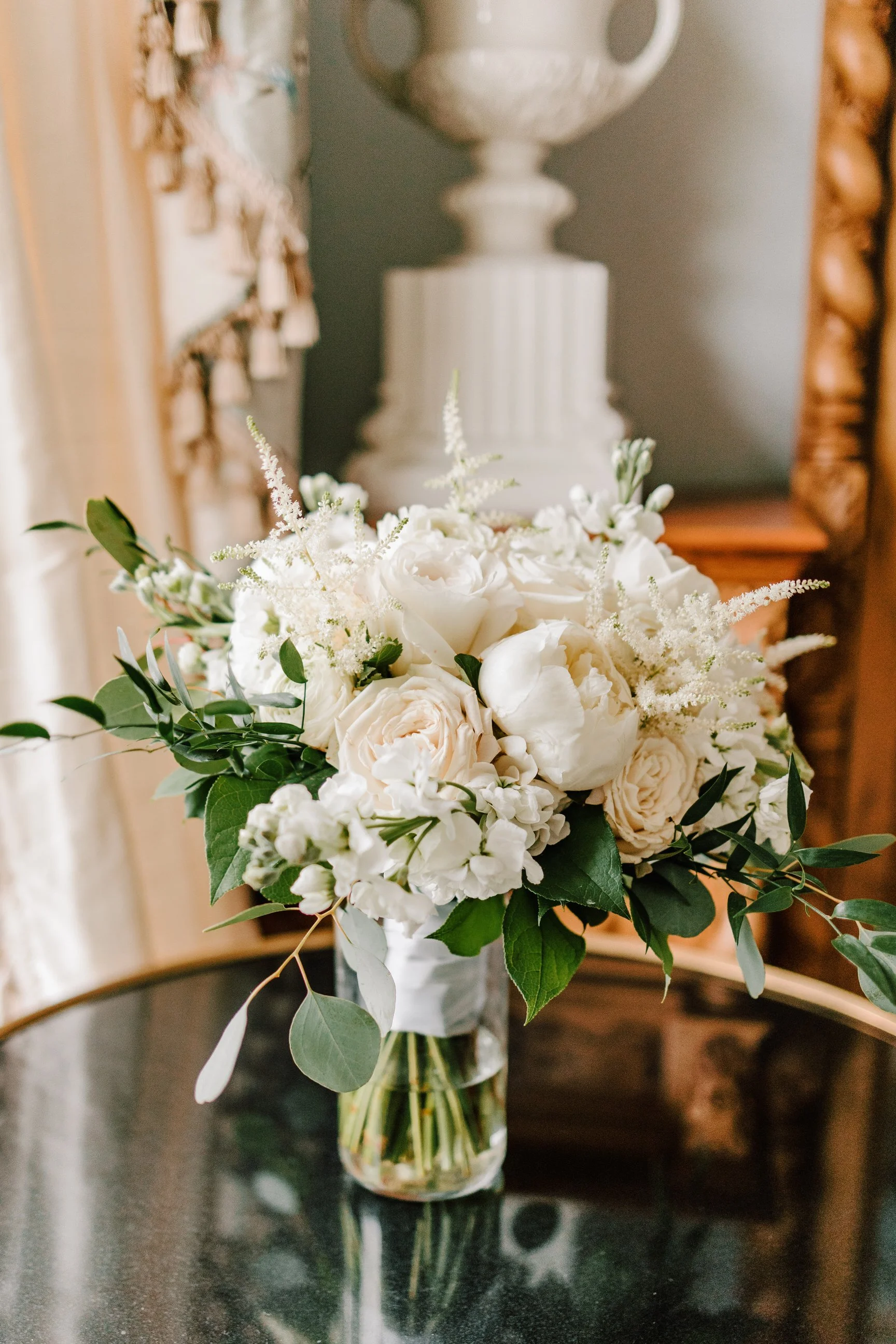 A bouquet of white flowers, including roses and peonies, arranged with greenery in a clear glass vase on a black table.