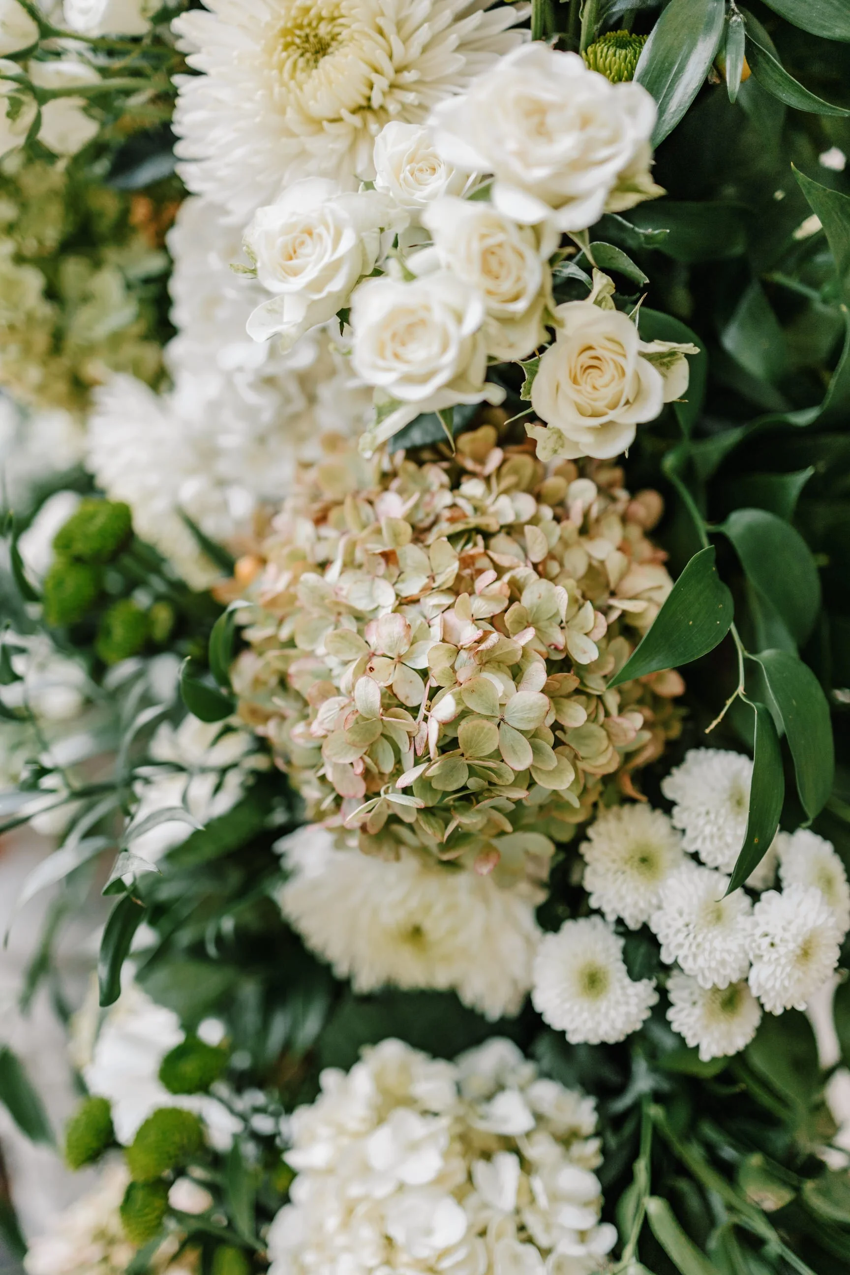 Close-up of a floral arrangement with white roses, hydrangeas, white chrysanthemums, and greenery.