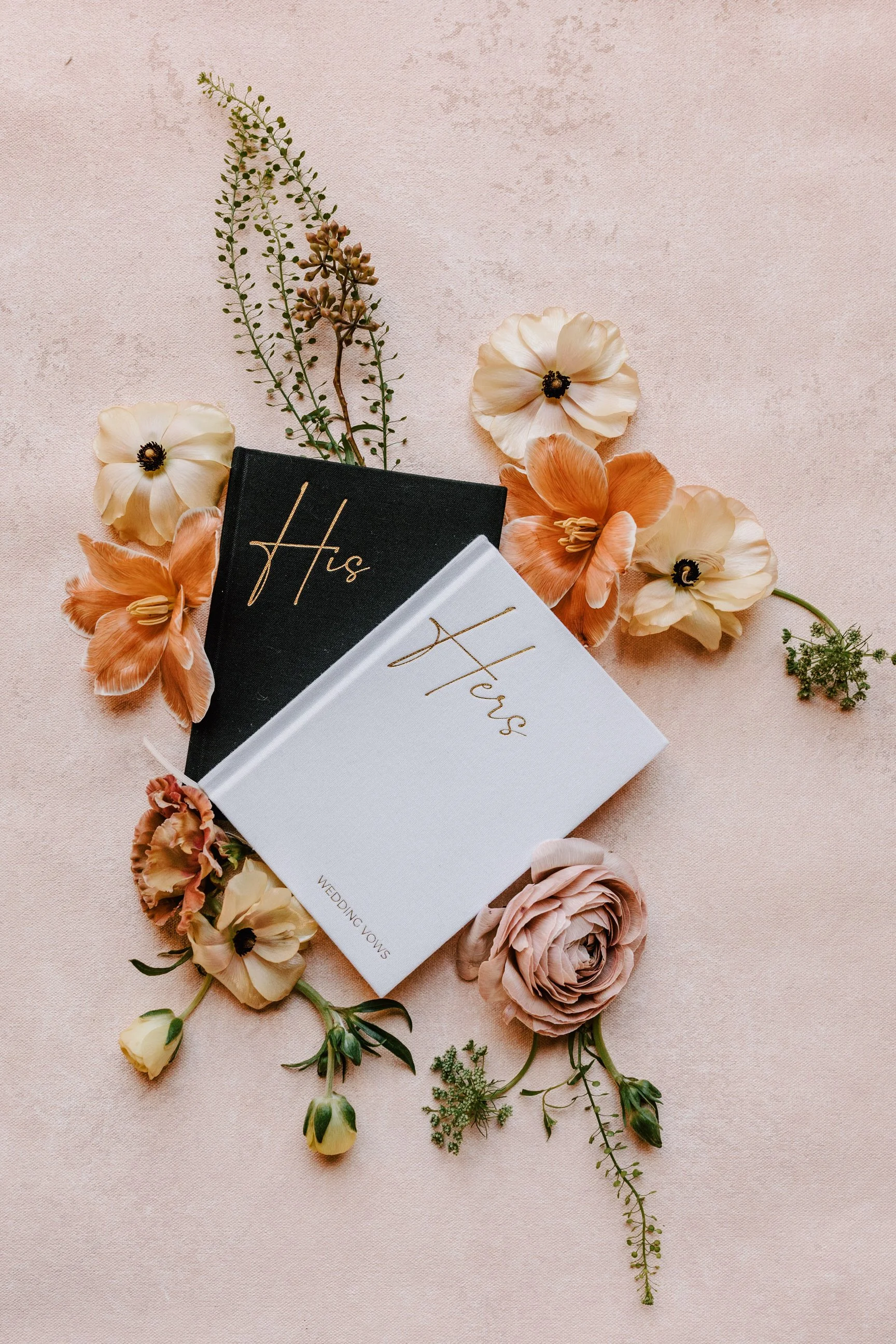 Wedding vow books labeled "His" and "Hers" surrounded by peach, cream, and blush flowers on a light pink background. Holly Hedge Estate Sharyn Louise Photo