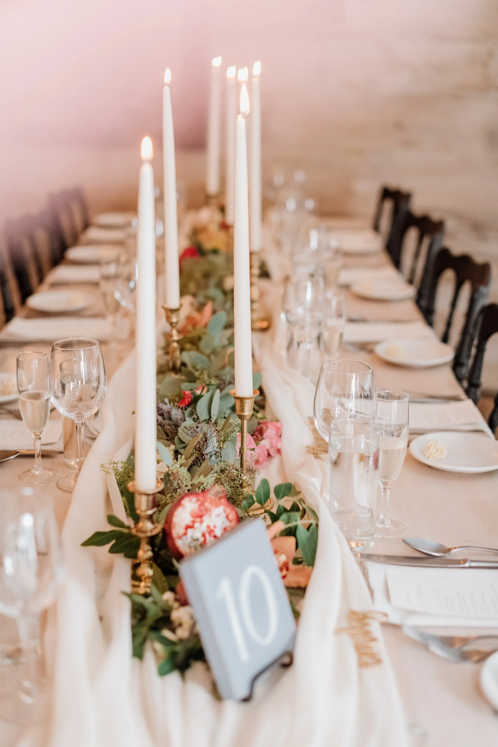 Elegant banquet table decorated with candles, greenery, and flowers for a wedding or special event, featuring a table number card '10' and glassware.