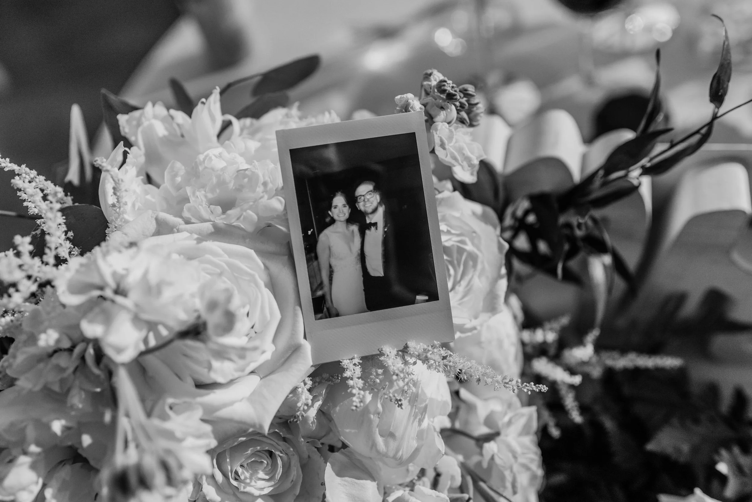 Black-and-white photo of a floral bouquet with a small picture of a man and woman in wedding attire placed among the flowers.