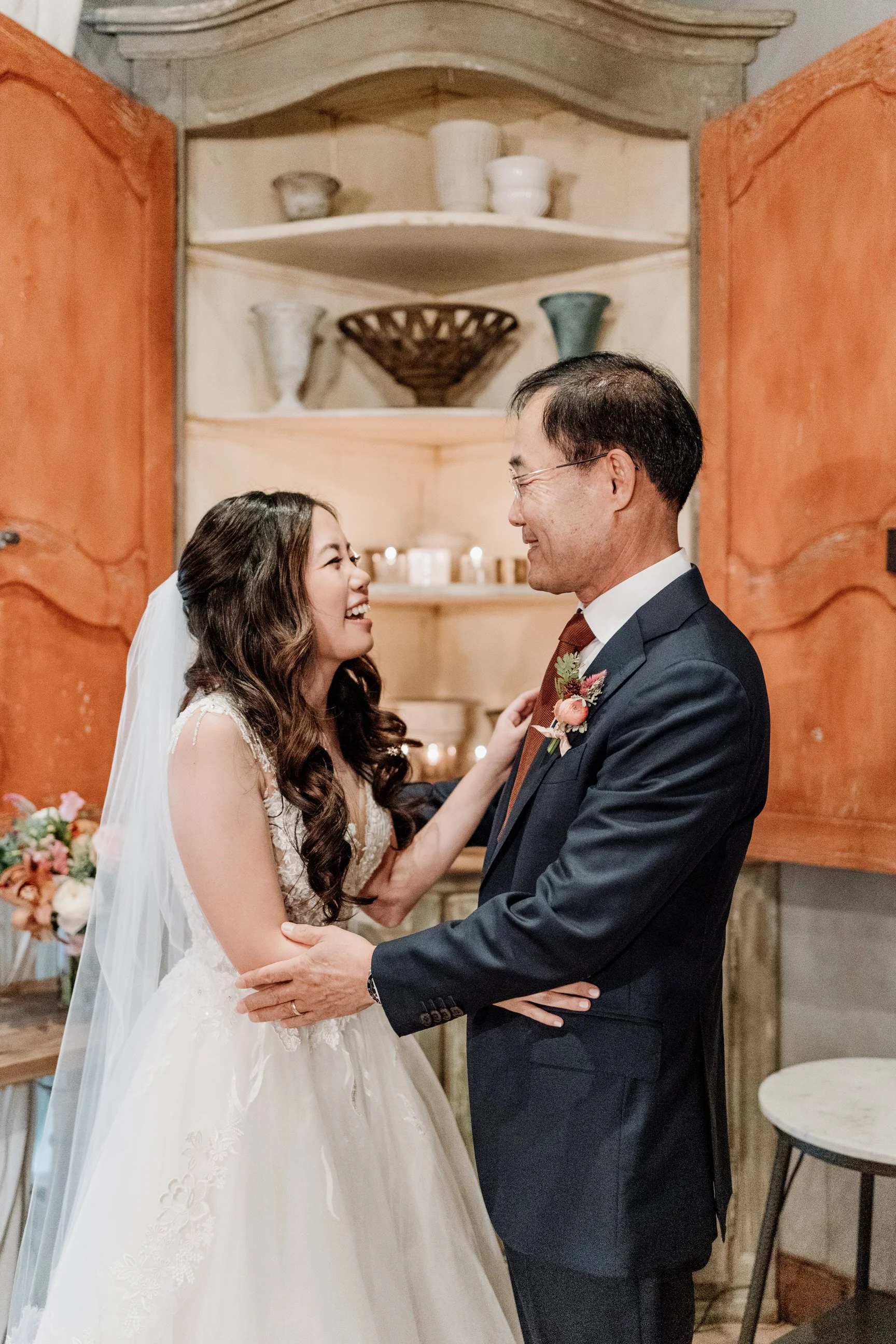 Bride and groom smiling and holding hands in a rustic indoor setting.