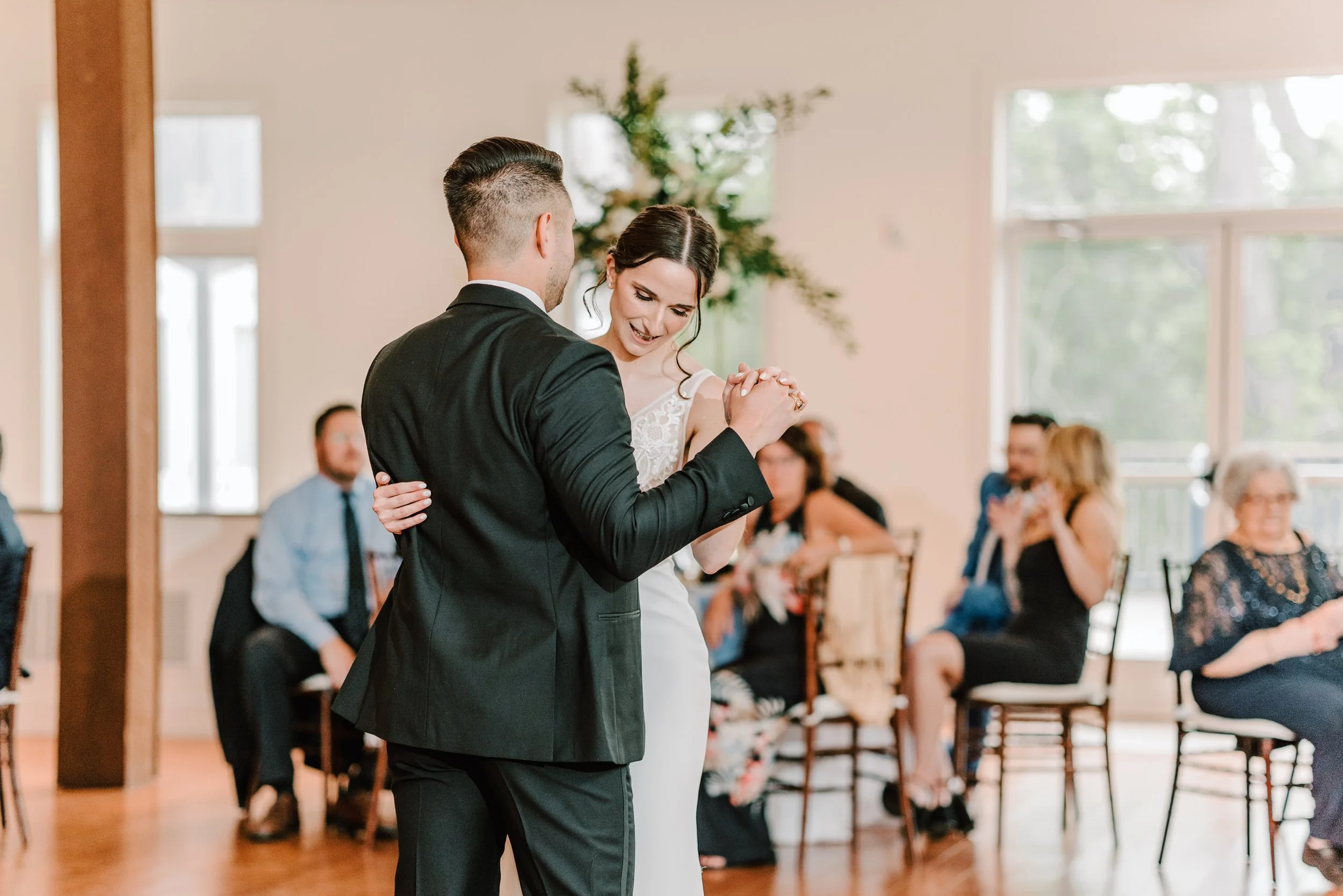 A bride and groom sharing their first dance at a wedding reception with guests watching in the background.
