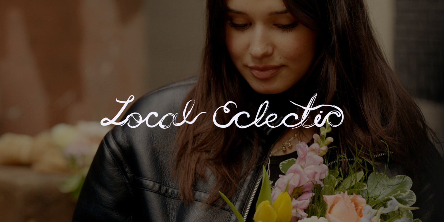A woman with brown hair wearing a black leather jacket holding a bouquet of pink, yellow, and white flowers, with the words "Local Collective" written in white cursive over the image.