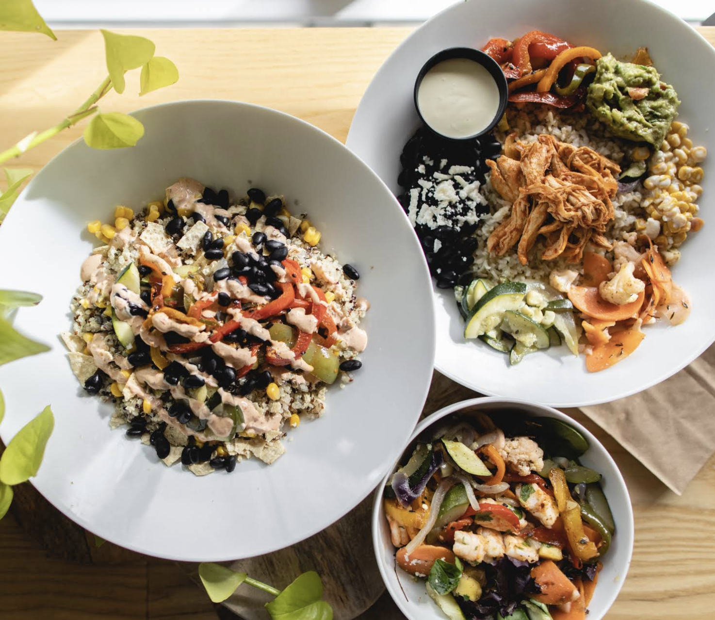 Three bowls and a plate of colorful vegan dishes with rice, vegetables, black beans, and sauce, on a wooden table.