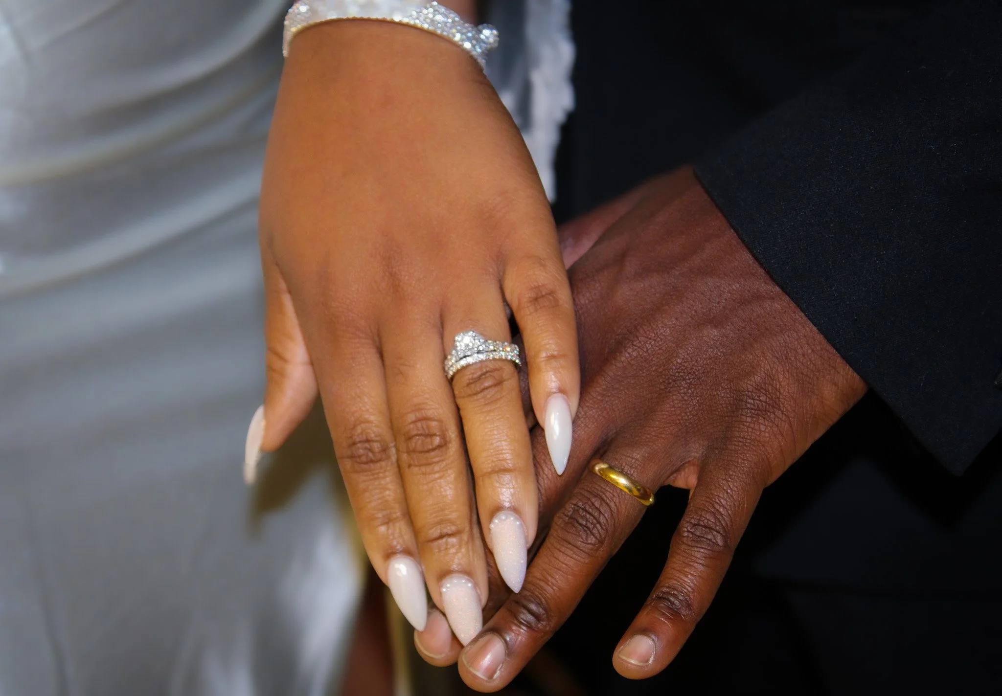 Indoor wedding ceremony setup with black chairs decorated with yellow sashes and small floral arrangements. The white ceiling is adorned with hanging green leaves. Large arched windows with white curtains line the walls, and a white draped backdrop decorated with greenery and orange fabric accents is at the front of the room.