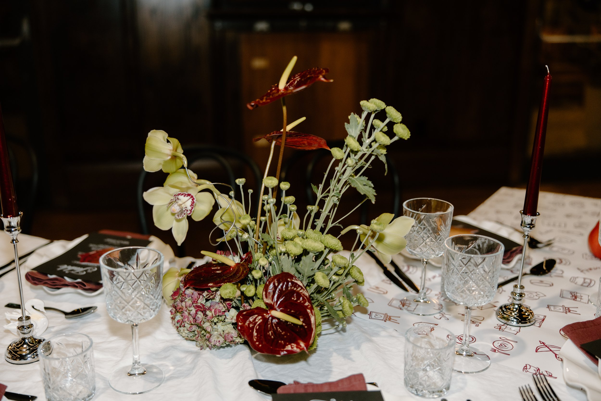 Elegant dining table with a floral centerpiece, glassware, candles, and place settings in a dimly lit room.