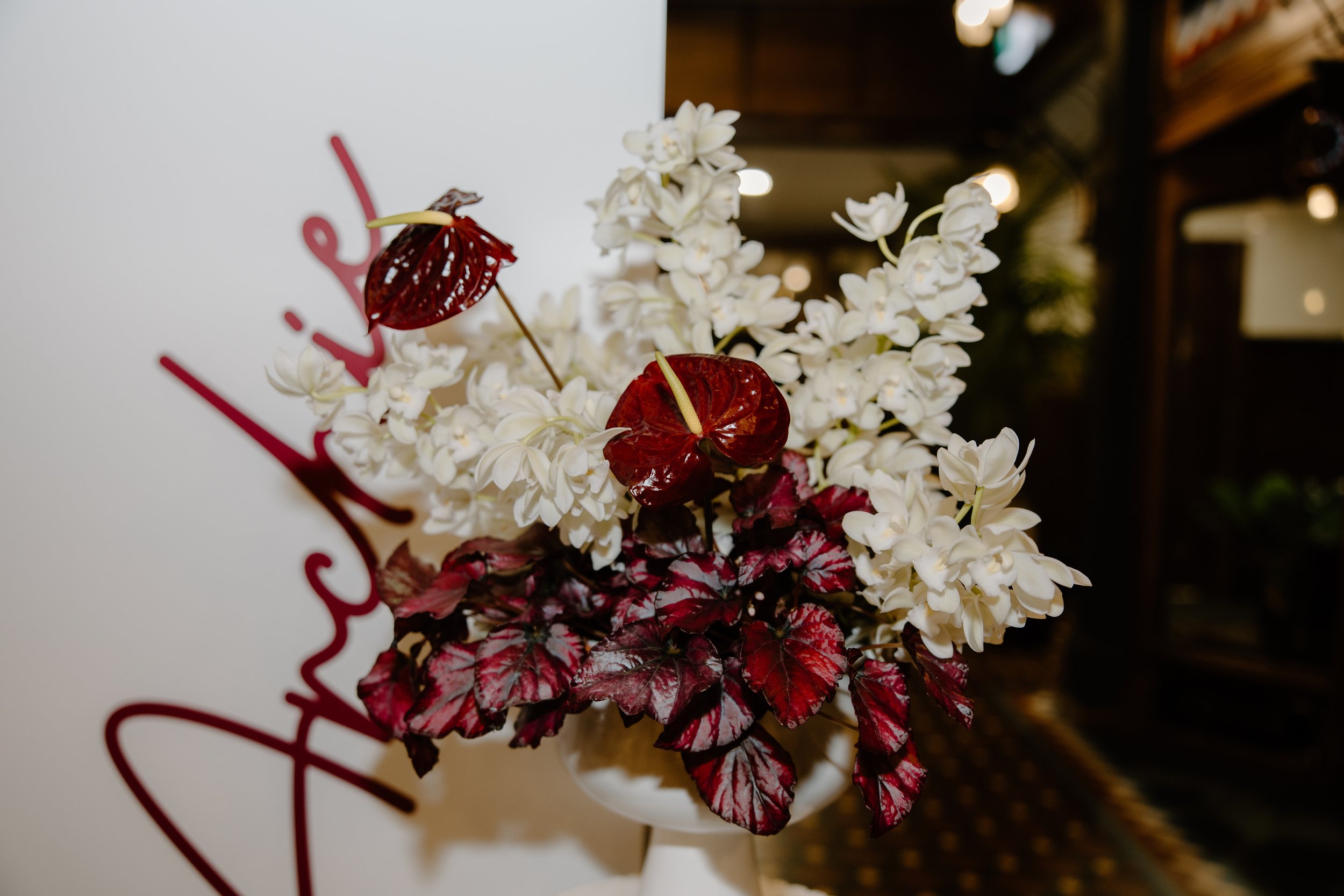 A floral arrangement with white flowers and dark red leaves against a white background with red text.