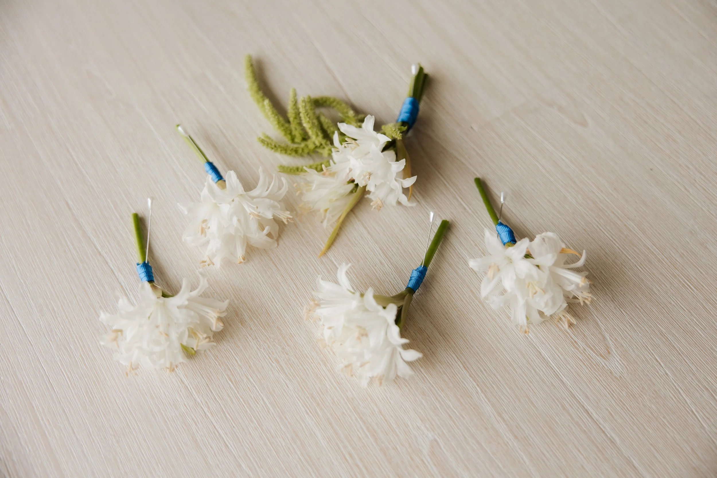 A flower crown made of white flowers and green stems, with blue and white pins attached, on a light wooden surface.