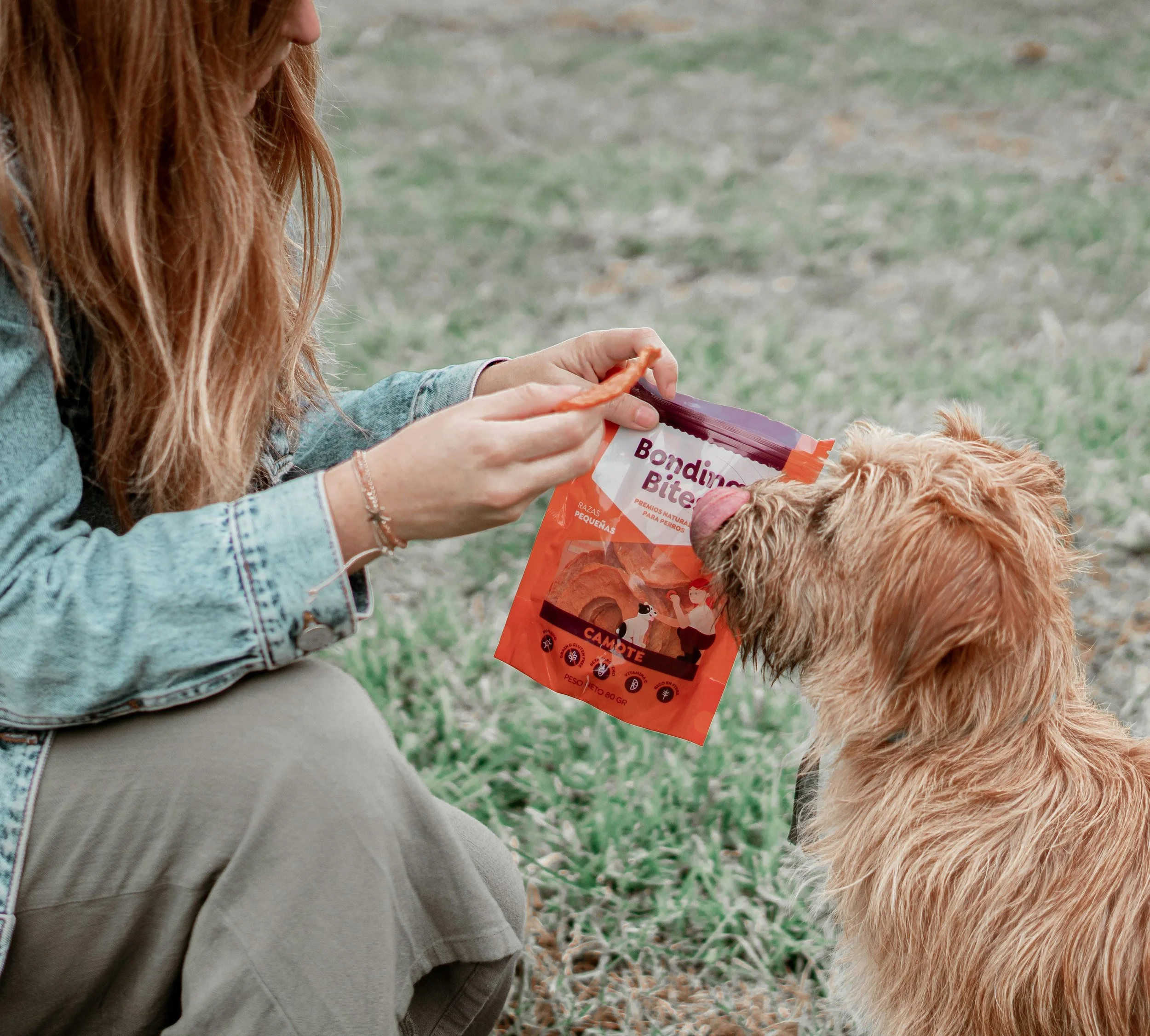 A woman offering a dog a treat from a package labeled Bonding Bites outdoors.