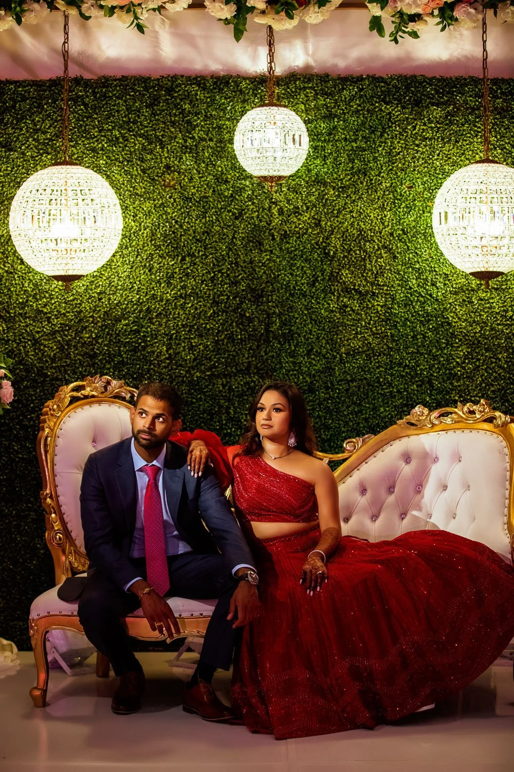 Bride and groom sitting on vintage couch in front of grassy backdrop