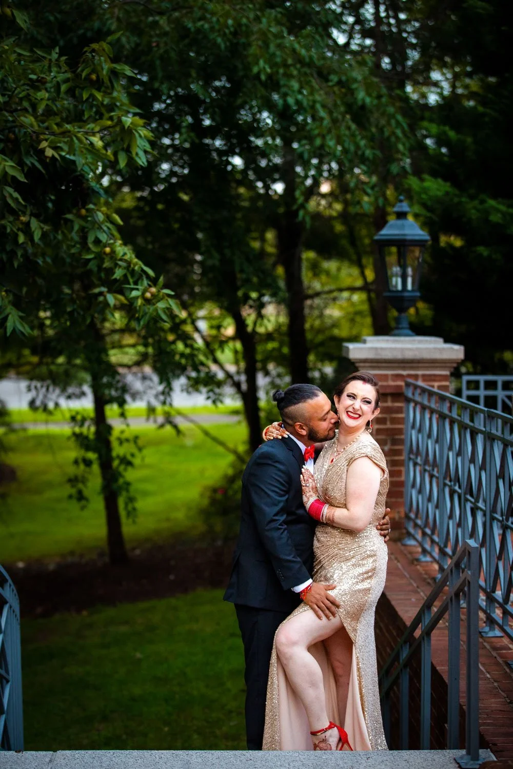 Groom kissing bride's neck posing on staircase at fusion wedding