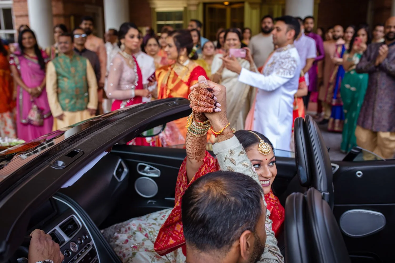 Bride and groom raise hands in triumph as they leave during the vidaai