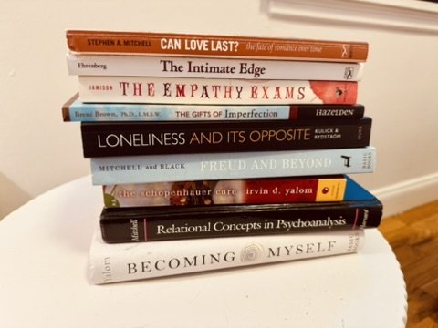 Stack of ten books on a white surface, with titles including "Can Love Last?", "The Intimate Edge", "The Empathy Exams", "Gifts of Imperfection", "Loneliness and Its Opposite", "Freud and Beyond", "The Chopinhauer Cure", "Relational Concepts in Psychoanalysis", and "Becoming Myself".