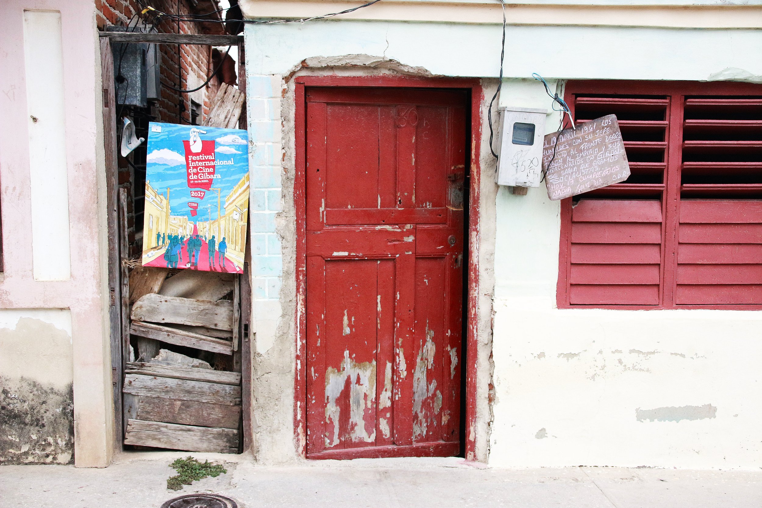 A poster promoting the Gibara Film Festival right next to the front of a house in critical state, showing one of the paradoxes of Cuba.| Credit: Reynaldo Cruz Diaz