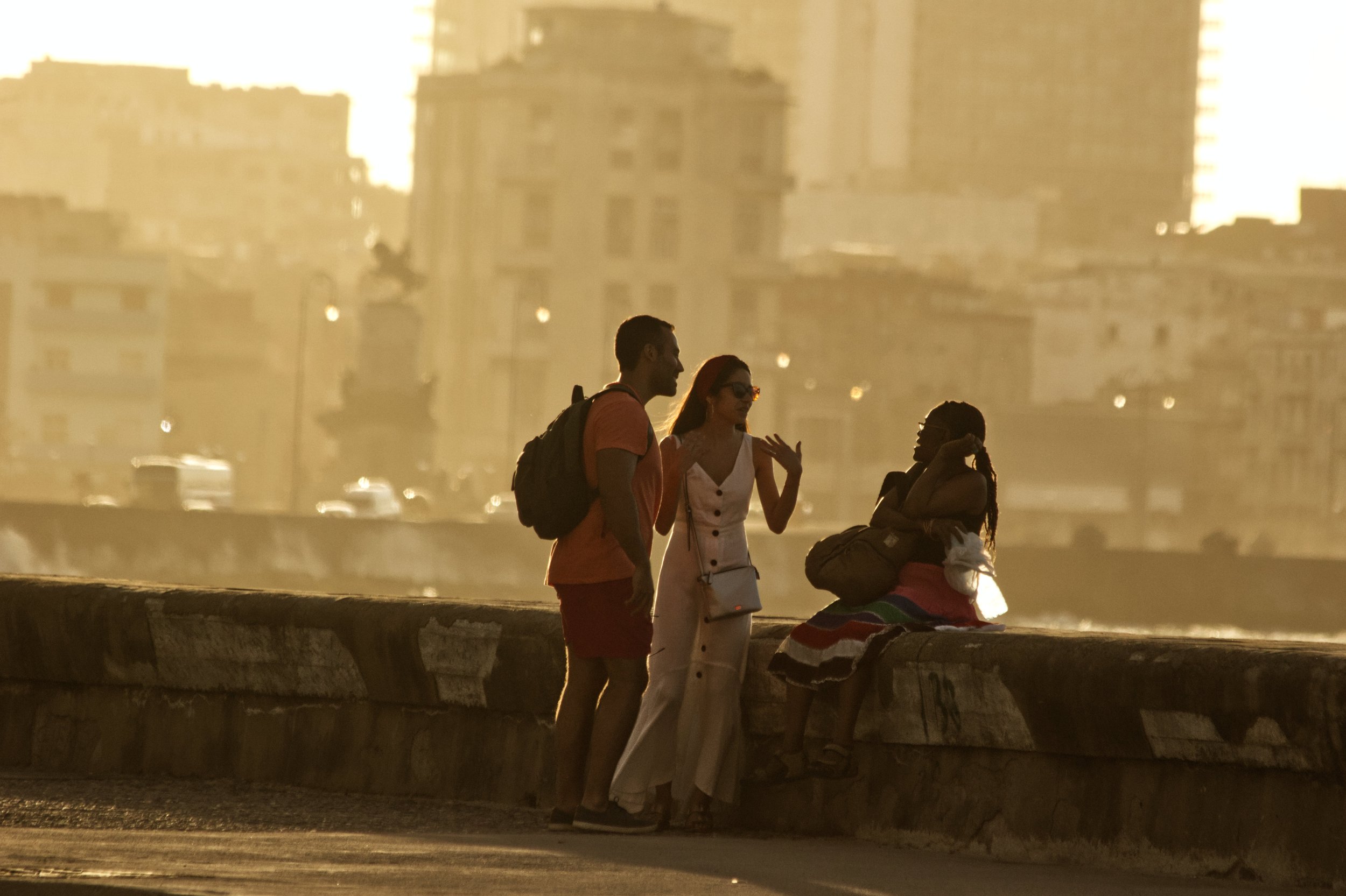 Two foreign travelers talk to a Cuban woman sitting on the Malecón (waterfront).| Credit: Reynaldo Cruz Diaz