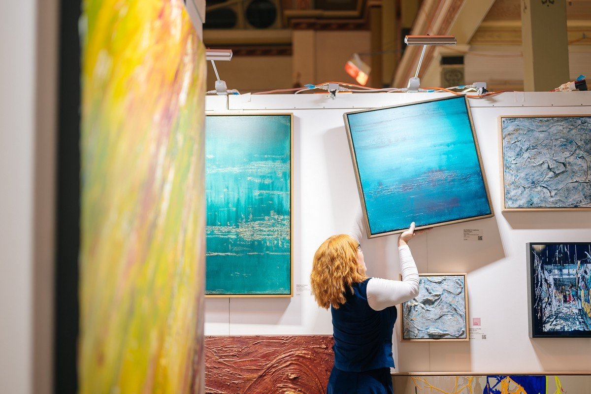 Person hanging a blue abstract painting in an art gallery.