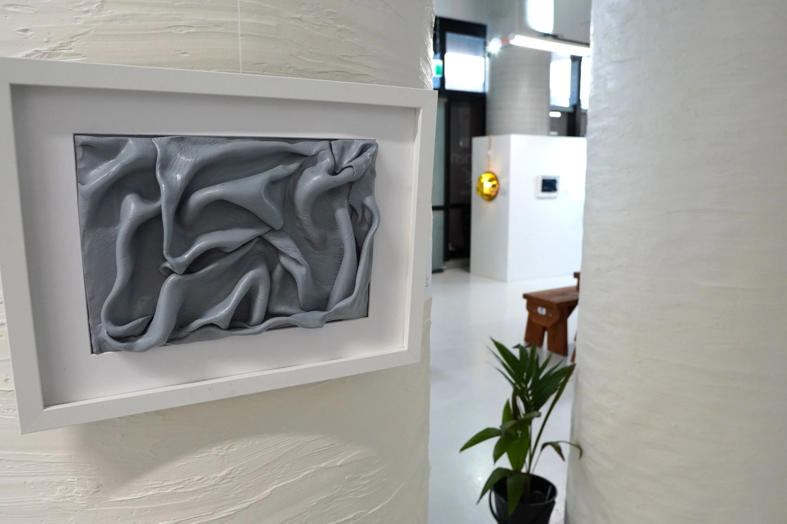 A framed artwork with a gray, textured, abstract design on a white wall in a modern interior space.