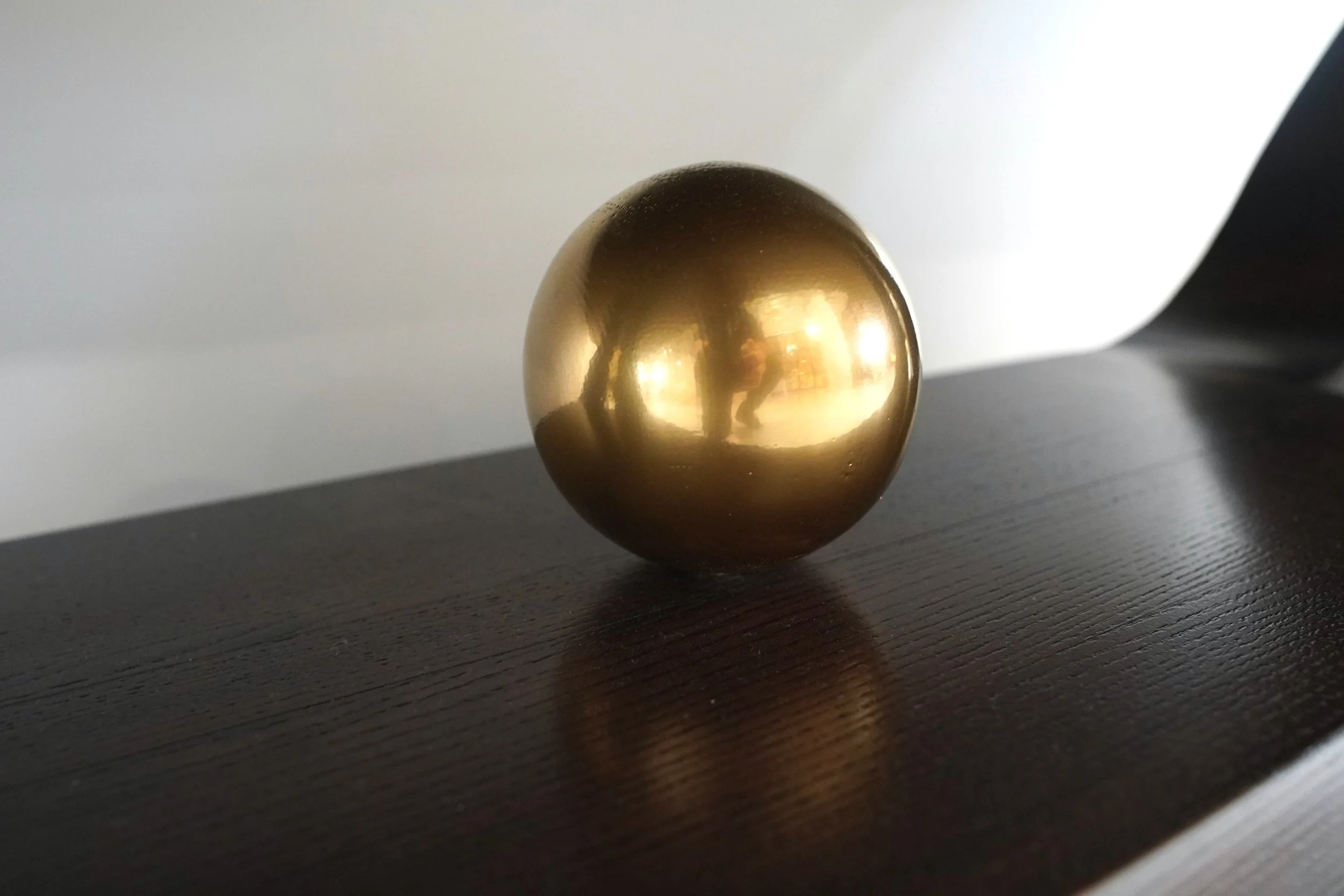 A shiny, gold-colored spherical object placed on a dark wooden surface with a white and black background.