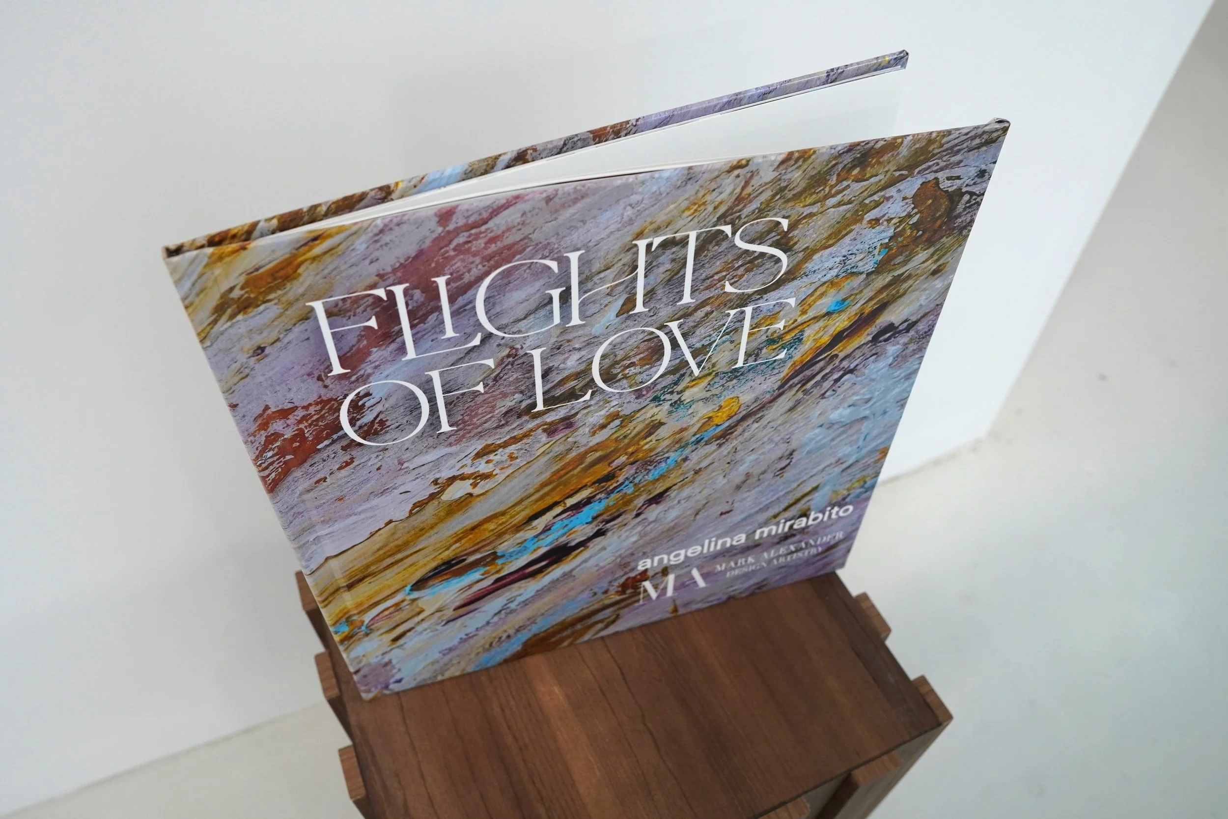 A book titled 'Flights of I Low' by Angelina Mirabito resting on a wooden stand against a white background.