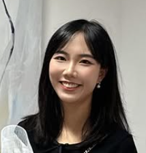 A woman with long black hair smiling in front of a light-colored background.