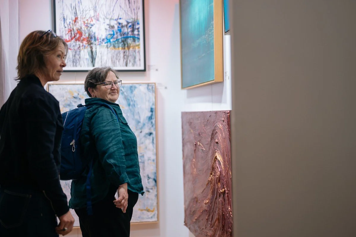 Two women viewing abstract paintings in an art gallery.