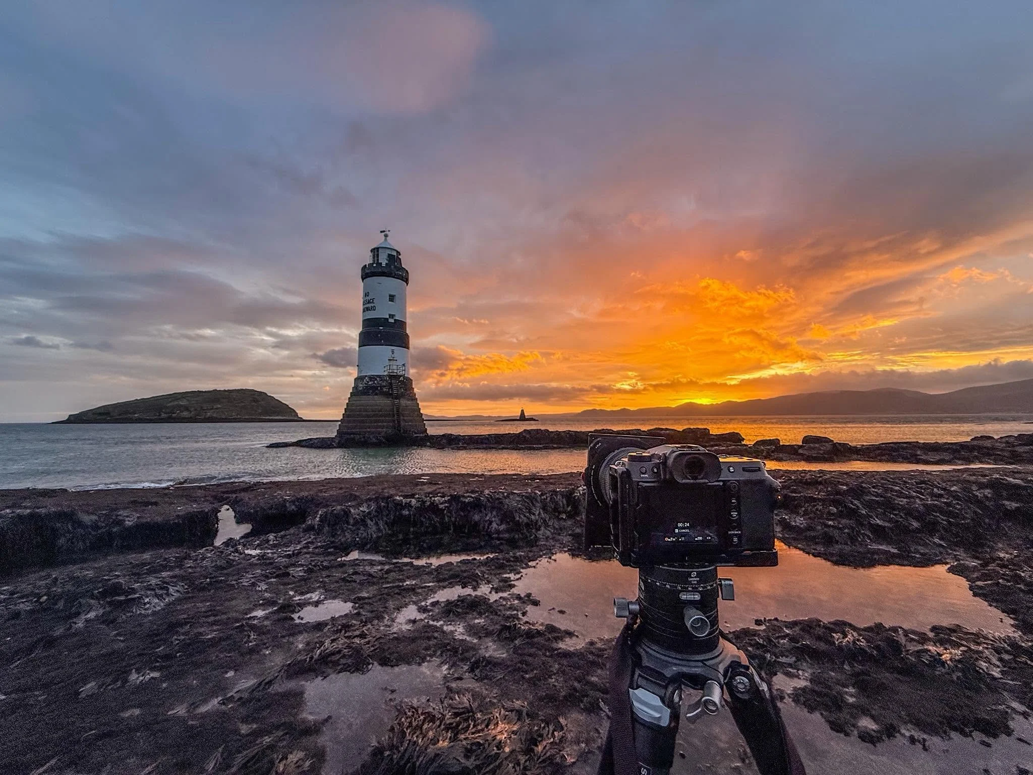Camera on a tripod photographing Penmon Lighthouse at sunset