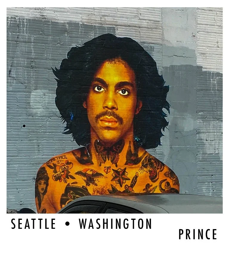 Street art mural of a man with black, curly hair and tattoos on his shoulders, set against a gray brick wall in Seattle, Washington. The mural includes text mentioning Prince.
