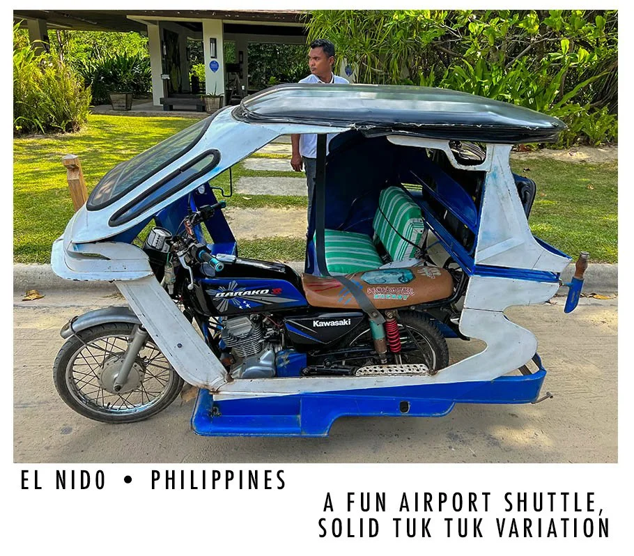 A tuk tuk with a motorbike inside, parked outside a building with green foliage in the background, in the Philippines.