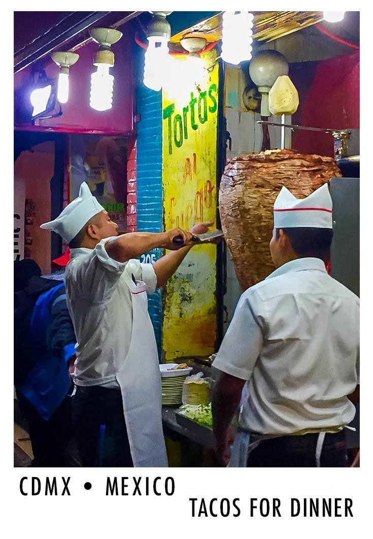 Two chefs preparing tacos at a street stall in Mexico City, with a large rotating spit of meat and a colorful sign that reads 'Tortas al Gordo'.