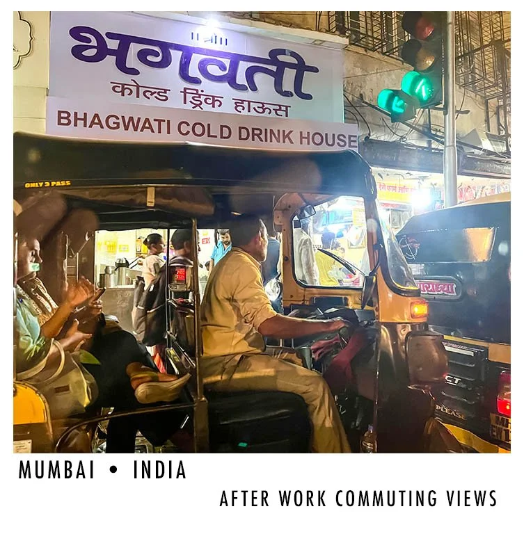 People riding an auto-rickshaw in Mumbai, India, after work, with a sign for Bhagwati Cold Drink House in the background and traffic lights showing green.